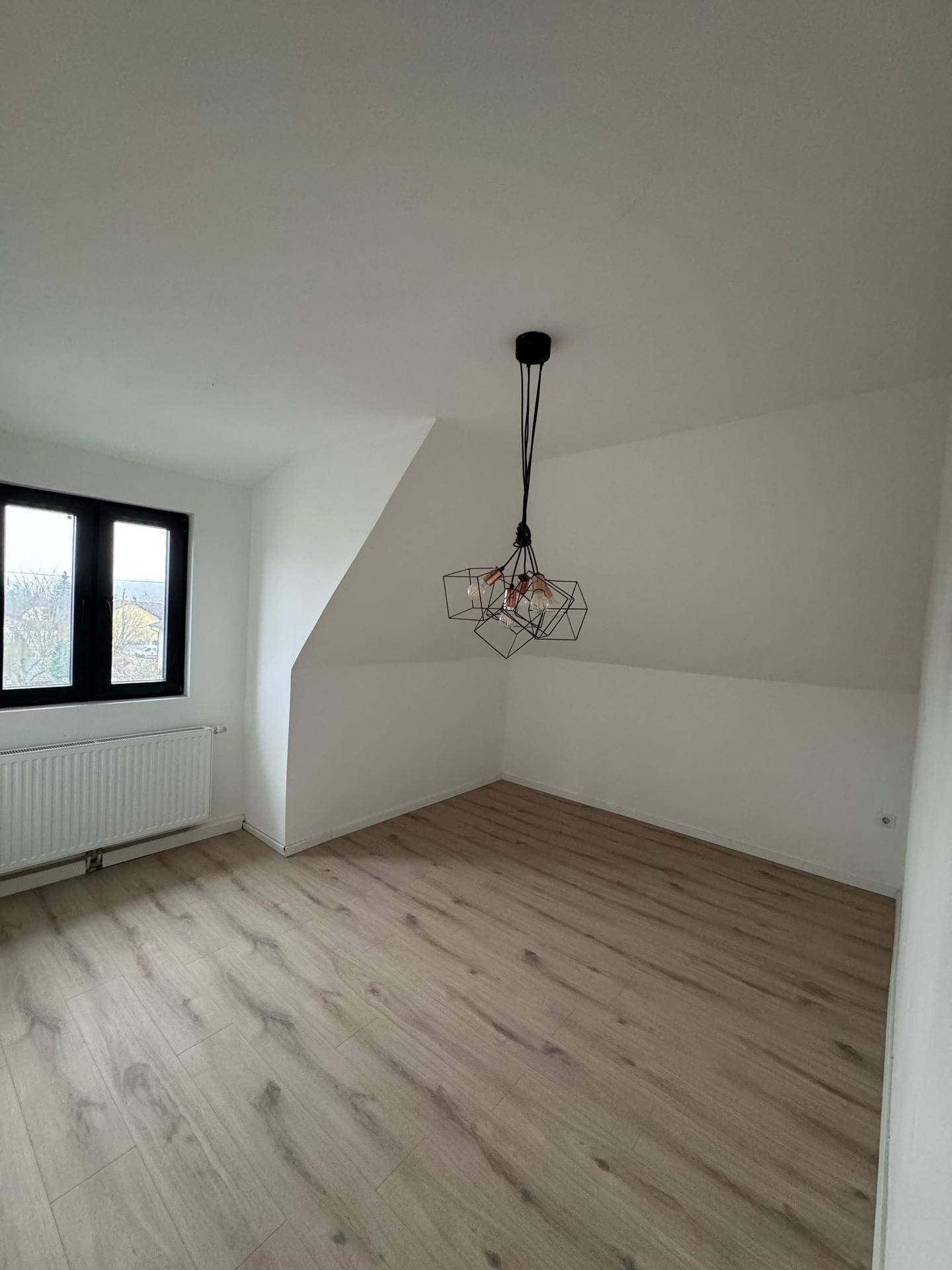 Dachgeschosszimmer mit Laminatboden, schrägen Wänden und modernem Deckenlicht.