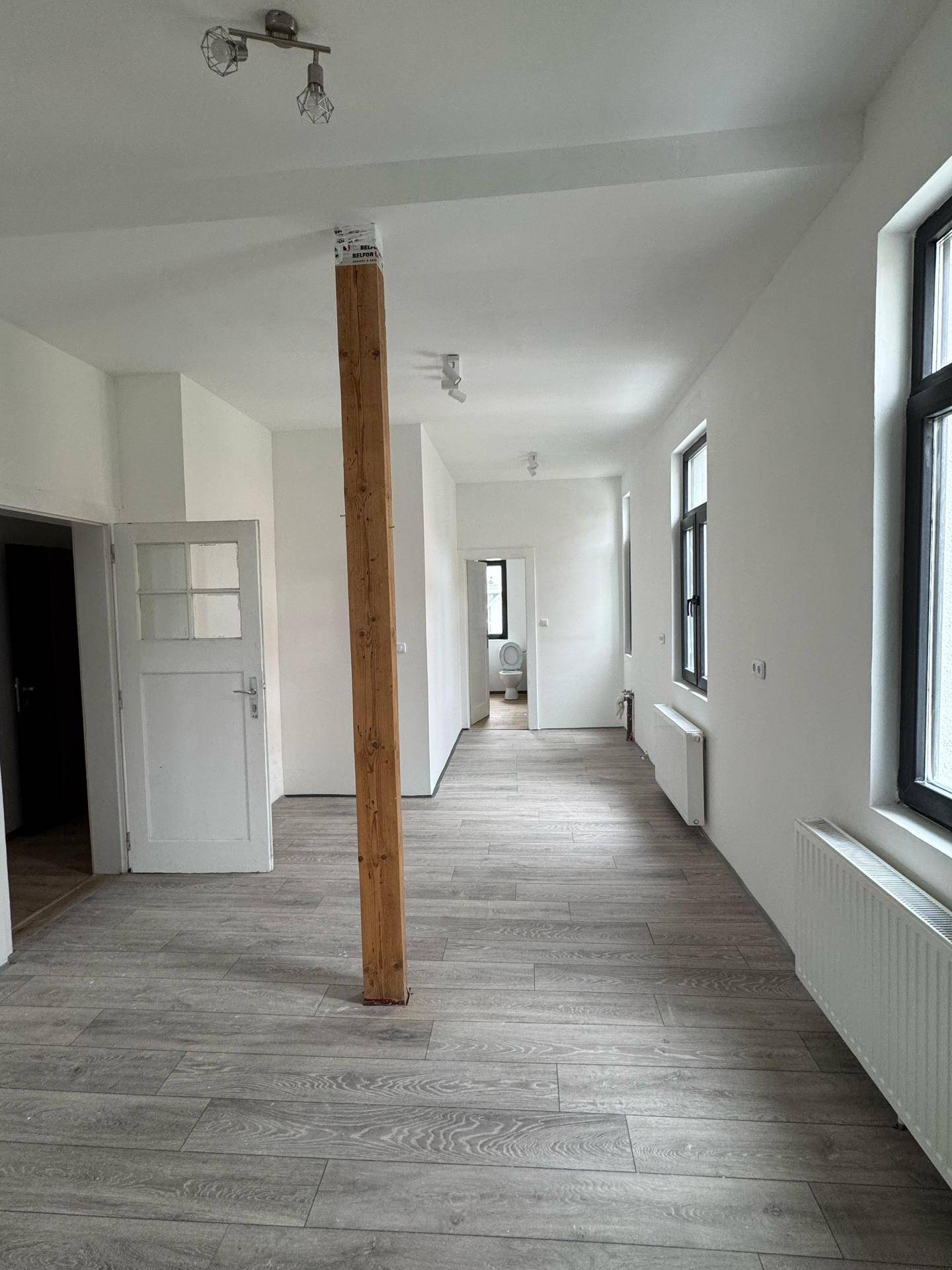 Langer, heller Wohnbereich mit Laminatboden, Holzbalken und mehreren Fenstern.