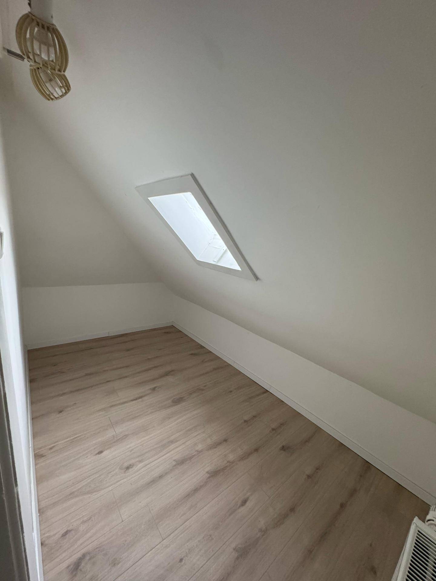 Helles Dachgeschosszimmer mit Laminatboden, schrägen Wänden und Dachfenster.