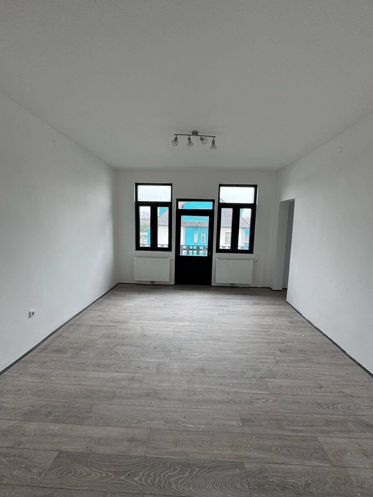 Geräumiger, heller Raum mit Laminatboden und mehreren Fenstern für viel Tageslicht.