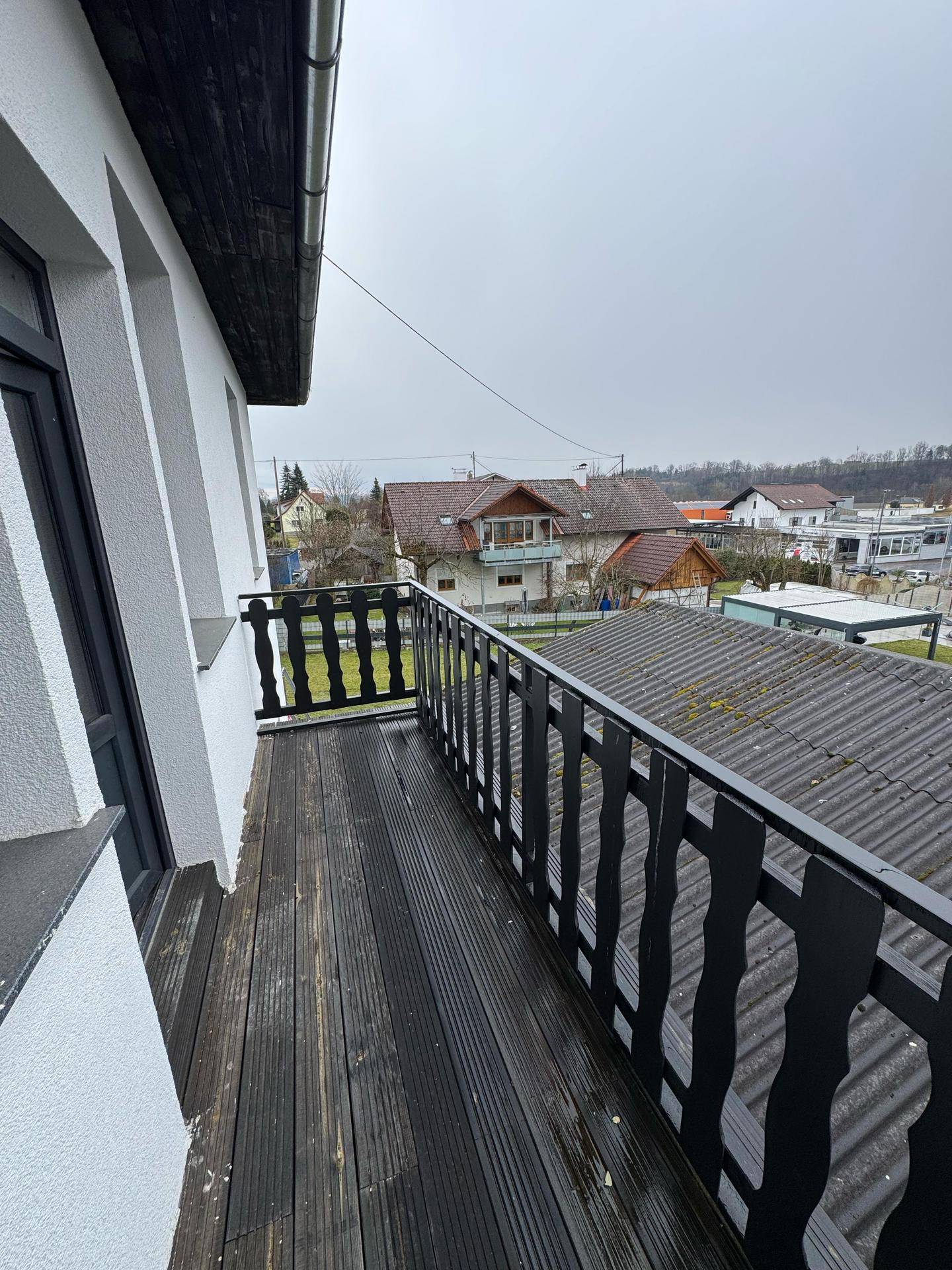 Balkon mit Holzboden und schwarzem Geländer, bietet Blick auf die Umgebung.