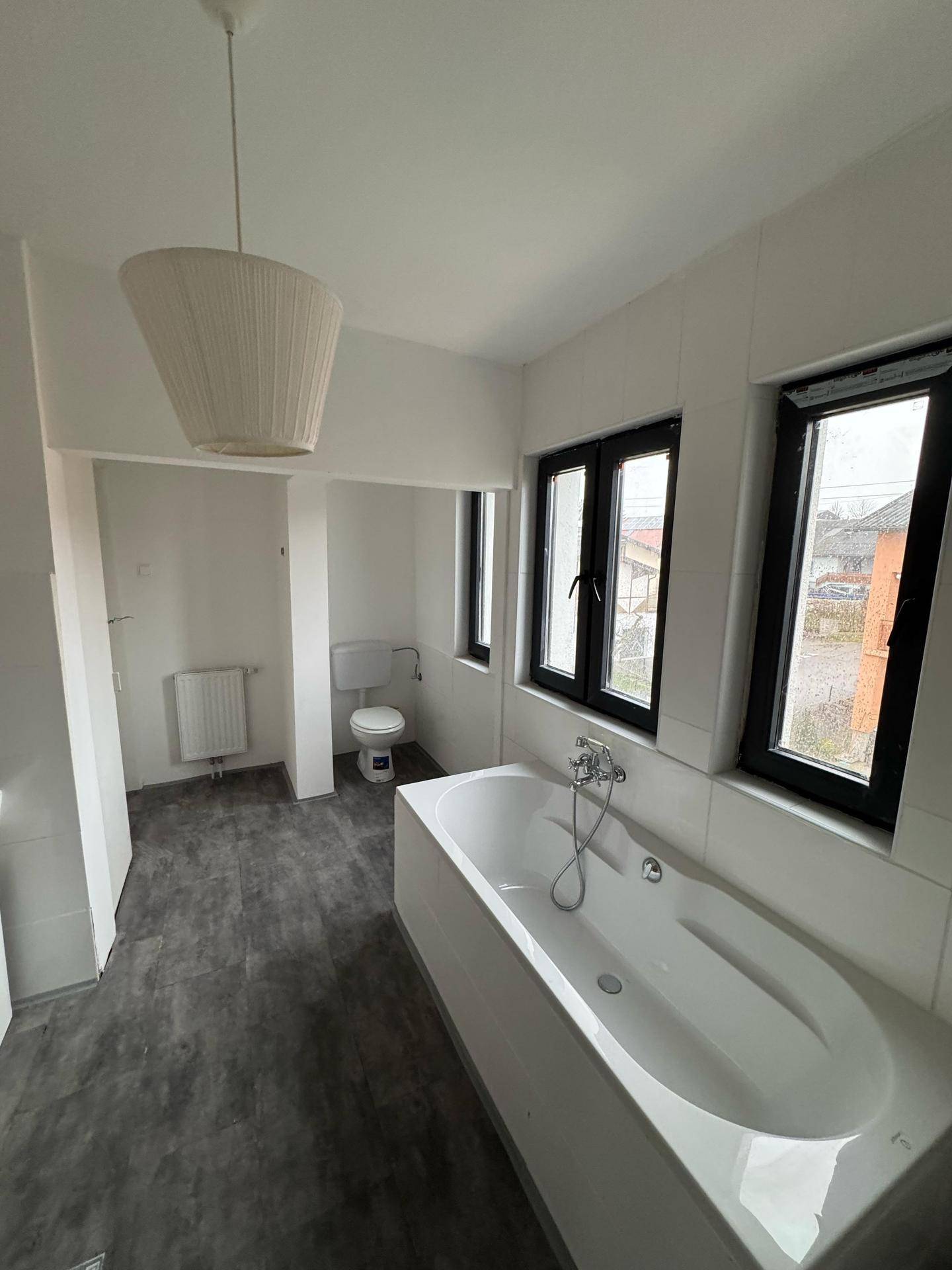 Geräumiges Badezimmer mit Badewanne, WC und mehreren Fenstern für Tageslicht.