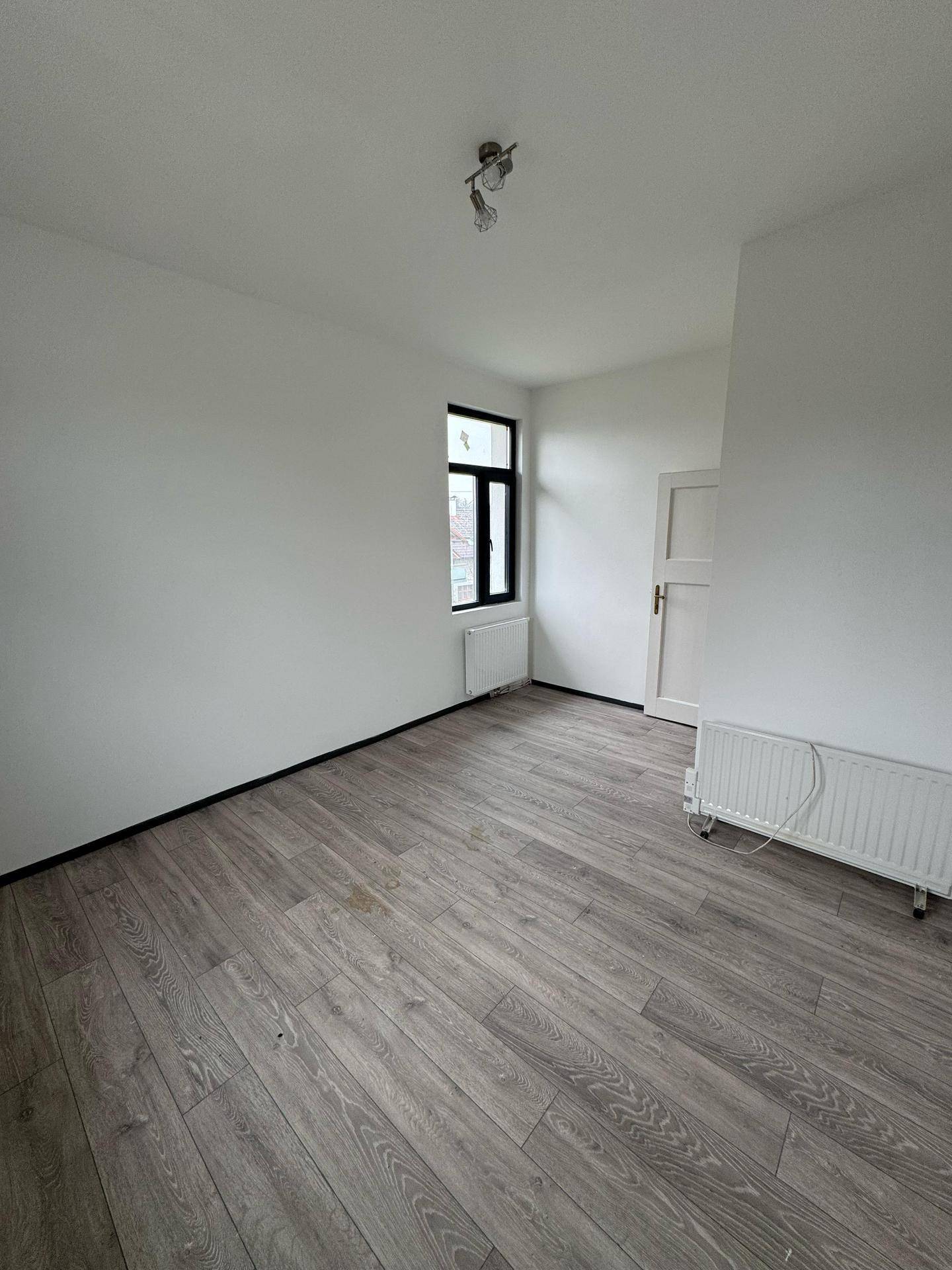 Helles Schlafzimmer mit Laminatboden, weißen Wänden und Heizkörper unter dem Fenster.