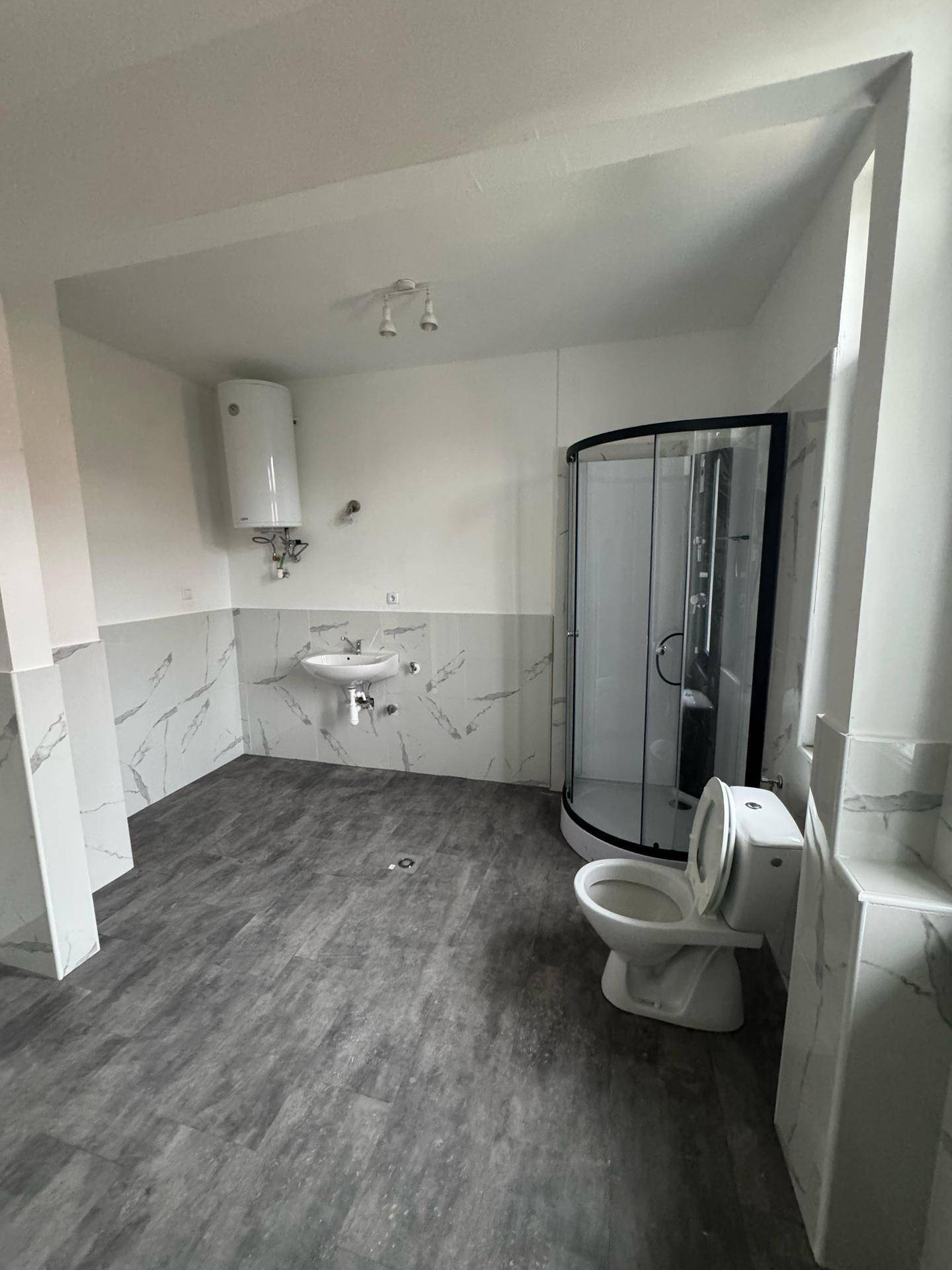 Badezimmer mit Duschkabine, WC, Waschbecken und Wandfliesen in Marmoroptik.