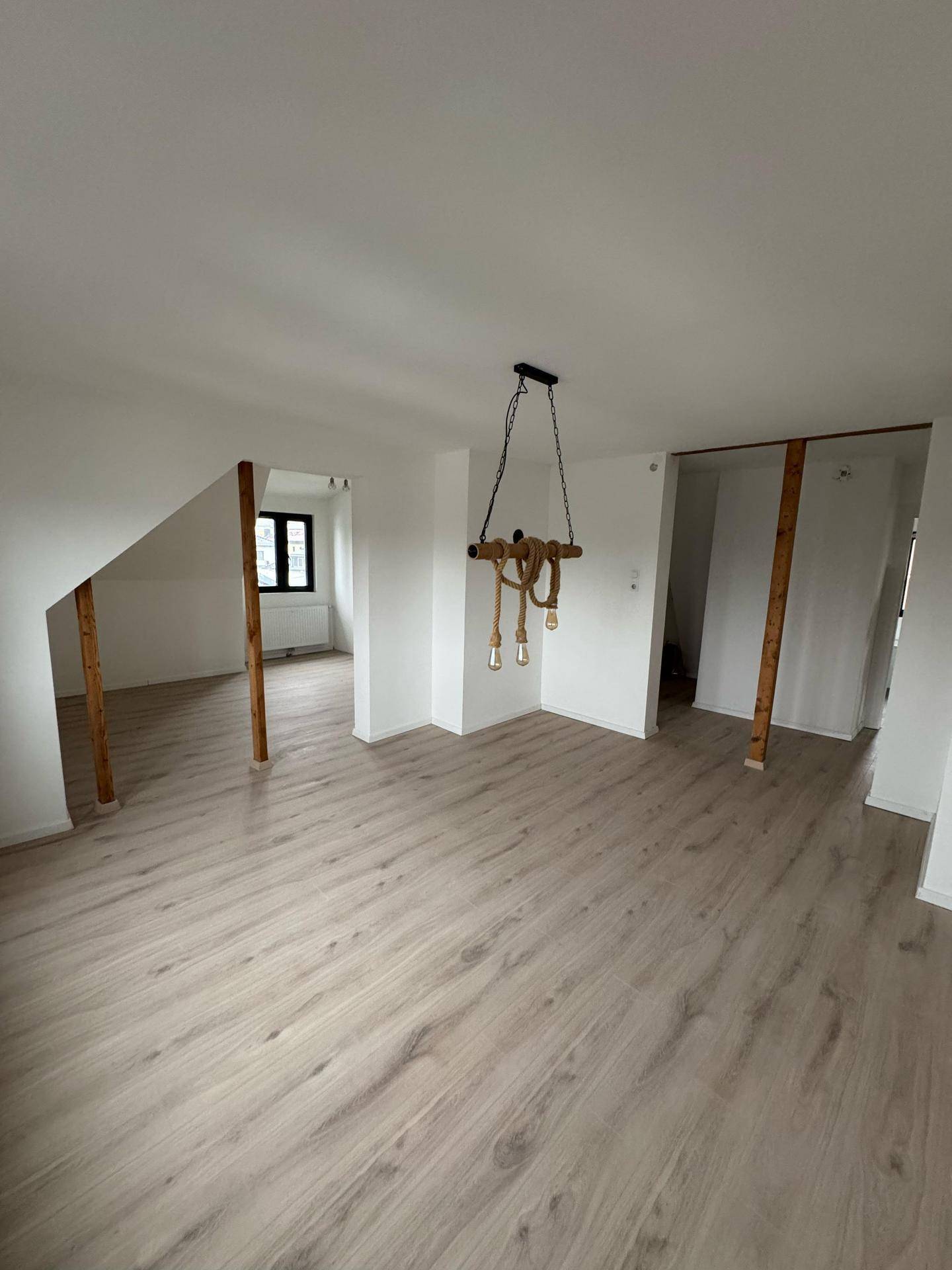 Offener Wohnbereich im Dachgeschoss mit Laminatboden, Holzbalken und rustikaler Beleuchtung.