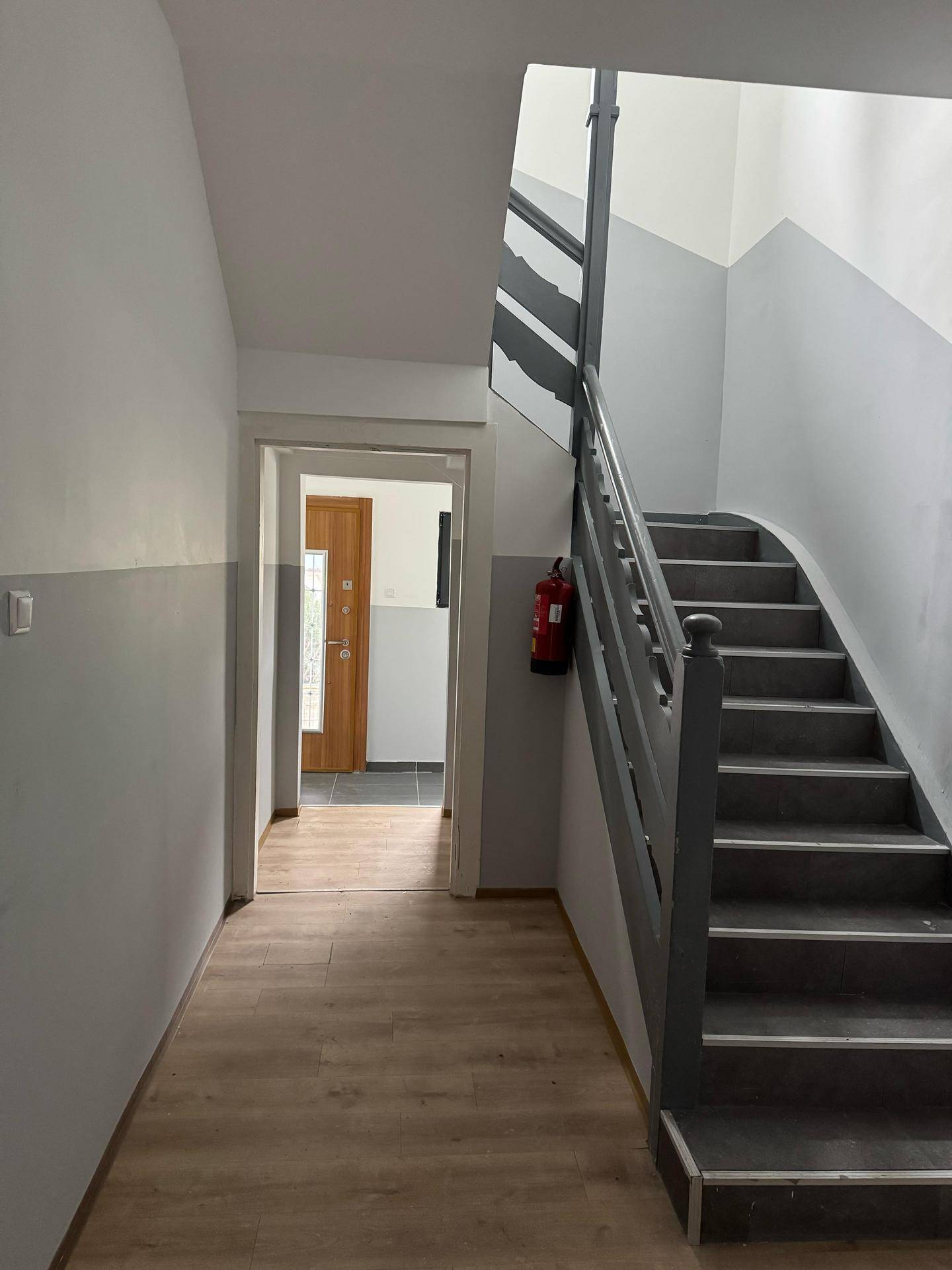 Treppenhaus mit Holztreppe, grau gestrichenen Wänden und Laminatboden im Flur.
