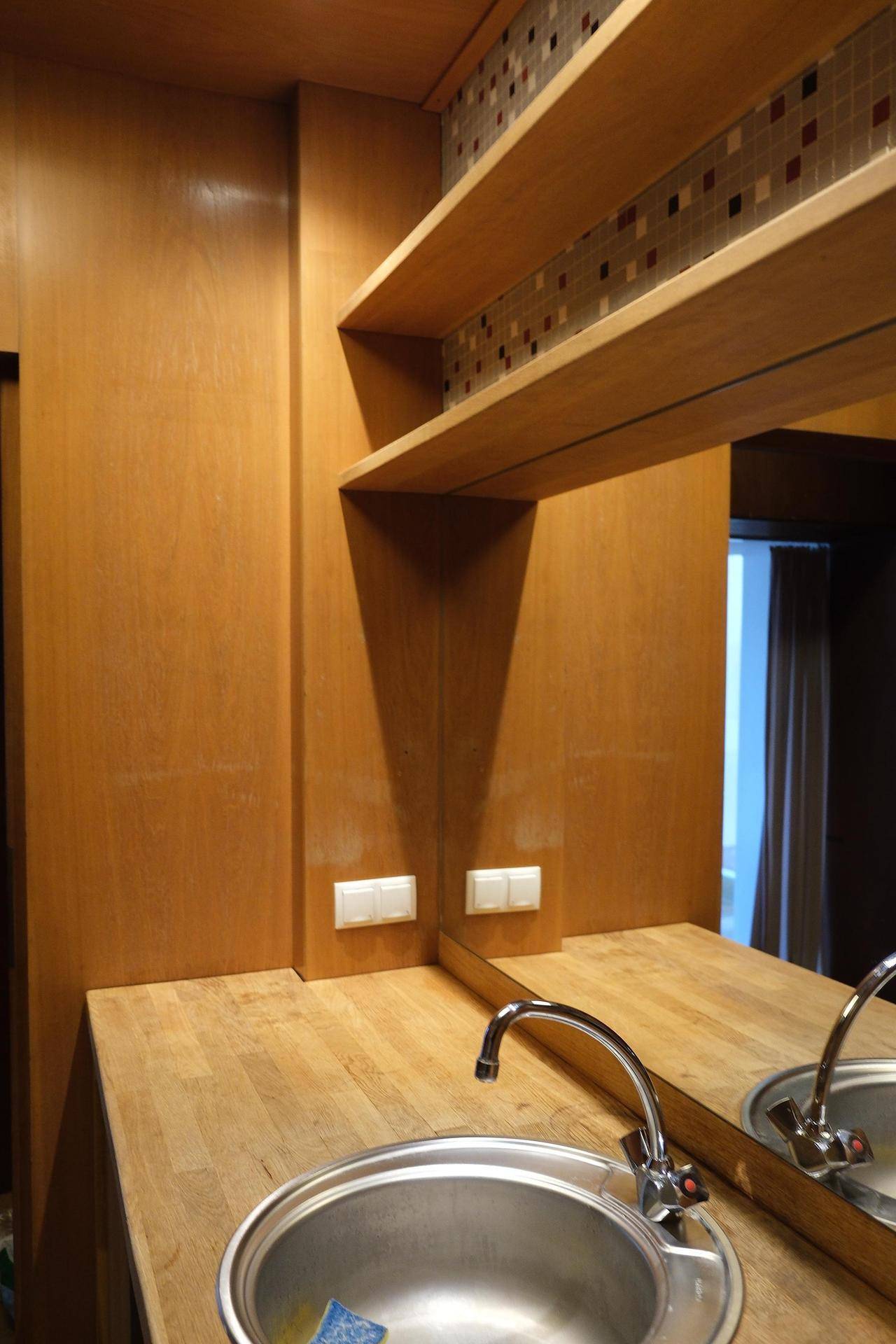 Waschbereich mit Holztheke, integriertem Waschbecken und Mosaikfliesen an der Wand, mit Regal.