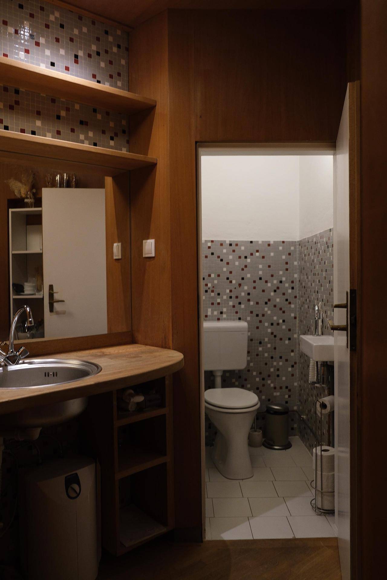 Kleine Gästetoilette mit Mosaikfliesen, WC und kleinem Waschbecken, funktional und sauber.