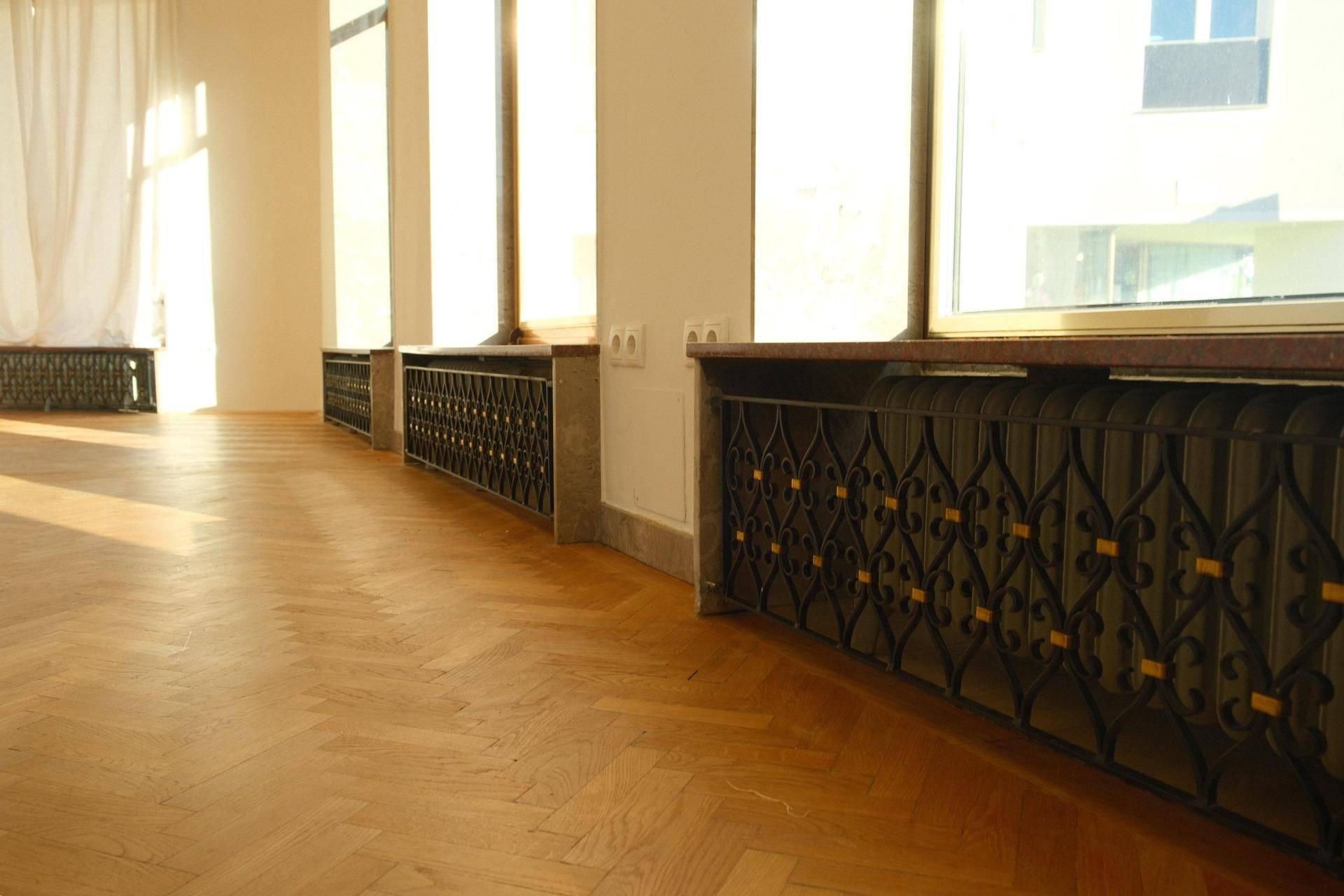 Detailansicht des Fischgrätparketts, der Fensterbänke und der kunstvollen Heizungsverkleidungen entlang der Fensterfront.
