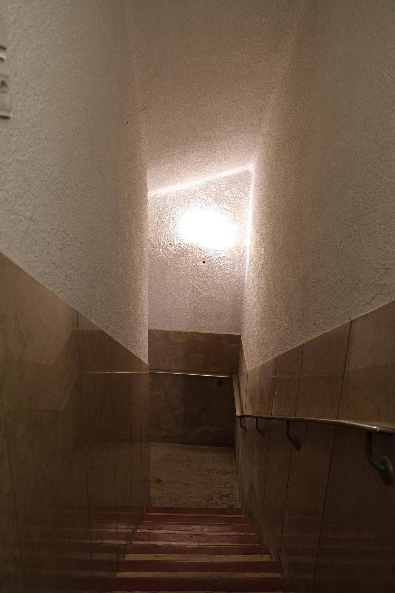 Treppenhaus mit gefliesten Wänden und Handläufen, das in einen unteren Bereich führt, einfach und funktional.