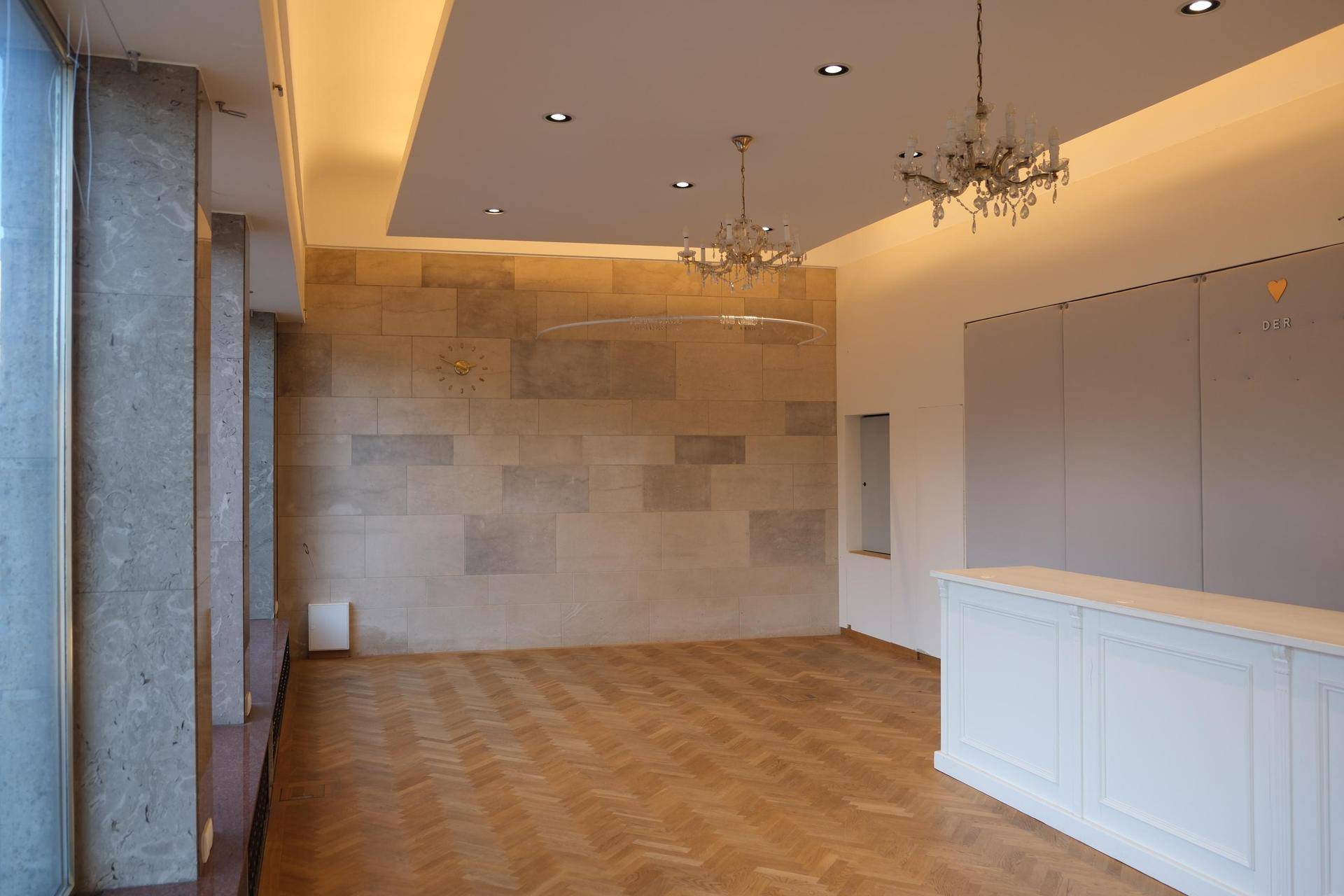 Weitläufiger Geschäftsraum mit Fischgrätparkett, einer markanten Steinwand und einer weißen Theke, gut beleuchtet.