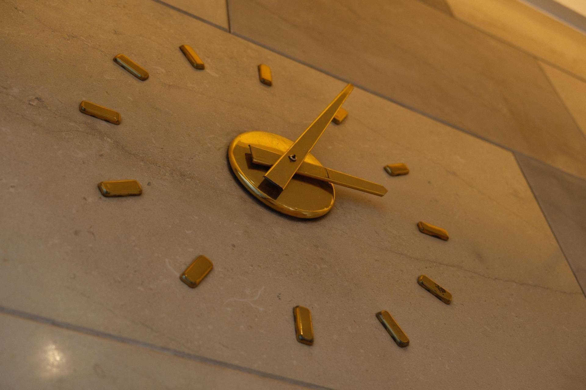 Nahaufnahme einer modernen, goldenen Wanduhr auf einer strukturierten Steinwand, die Eleganz verleiht.