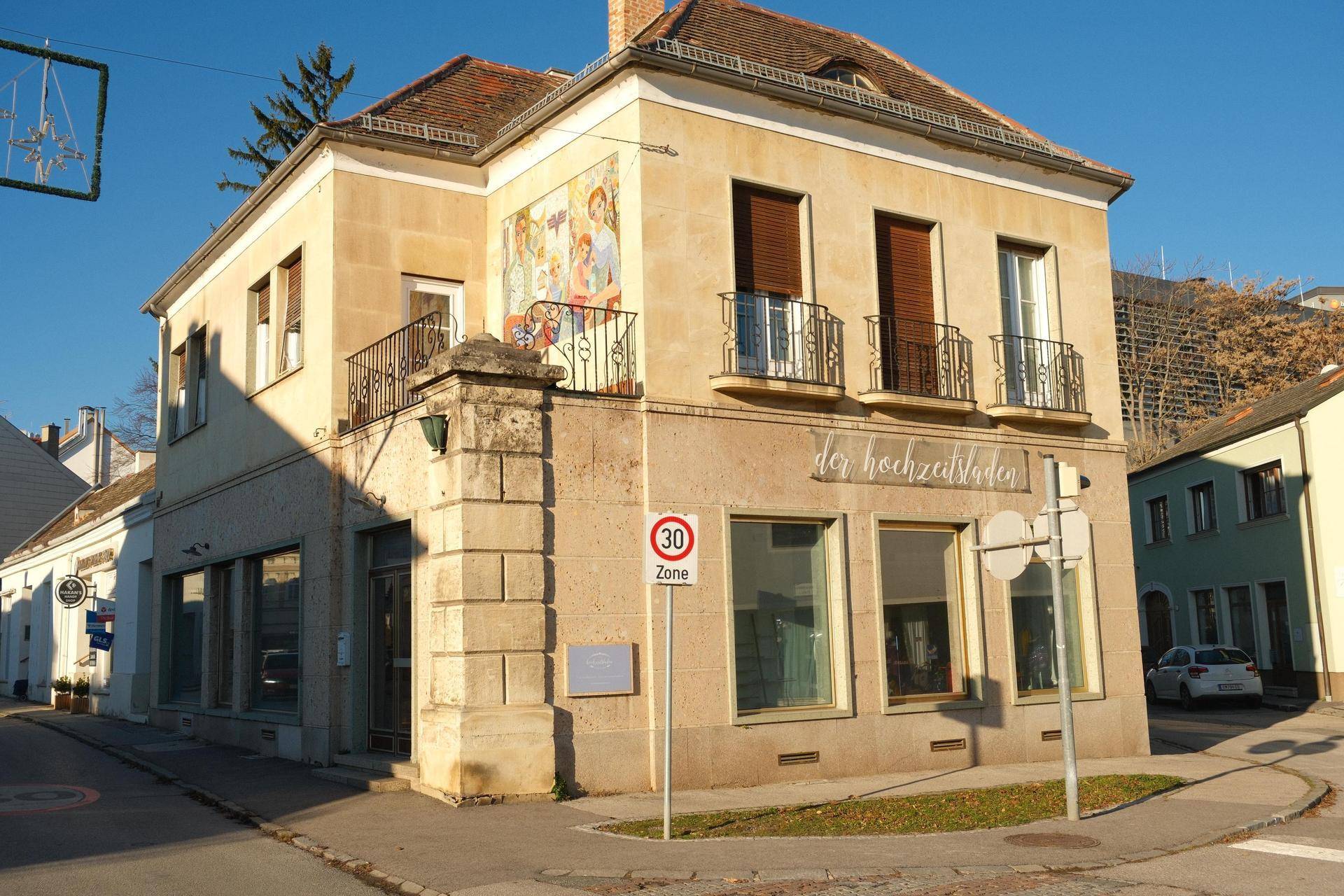 Historisches Eckgebäude mit Balkonen, großen Fenstern und einer bemalten Fassade, an einer belebten Straße gelegen.