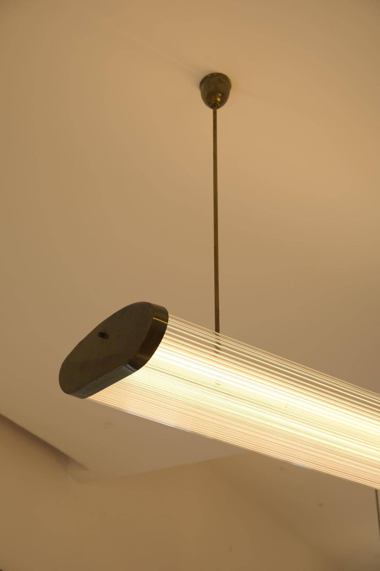 Nahaufnahme einer modernen, länglichen Hängelampe mit geriffelter Glasstruktur, die warmes Licht spendet.