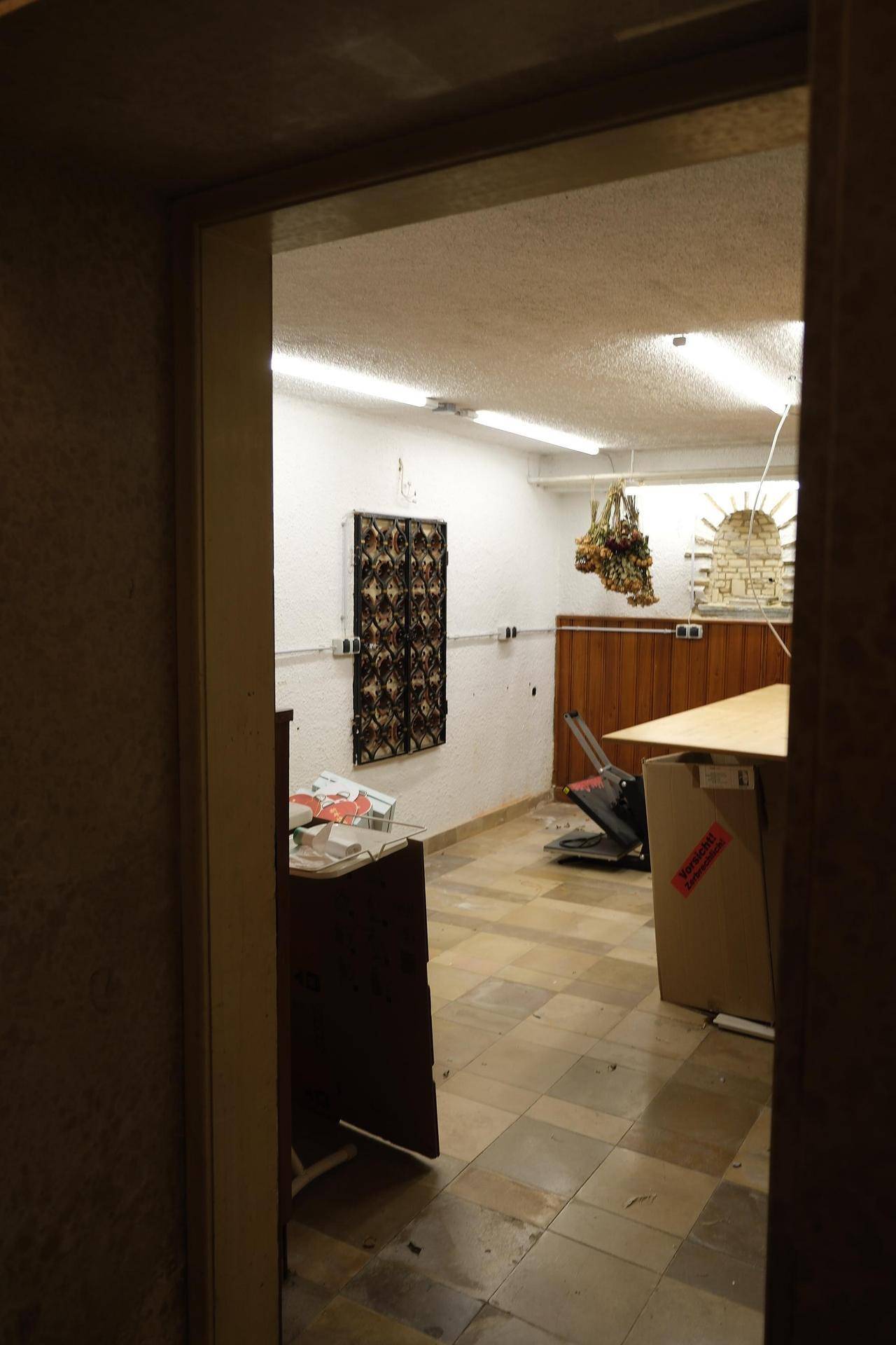 Kellerraum mit Fliesenboden und einfacher Beleuchtung, der als Lagerfläche oder Werkstatt genutzt werden kann.