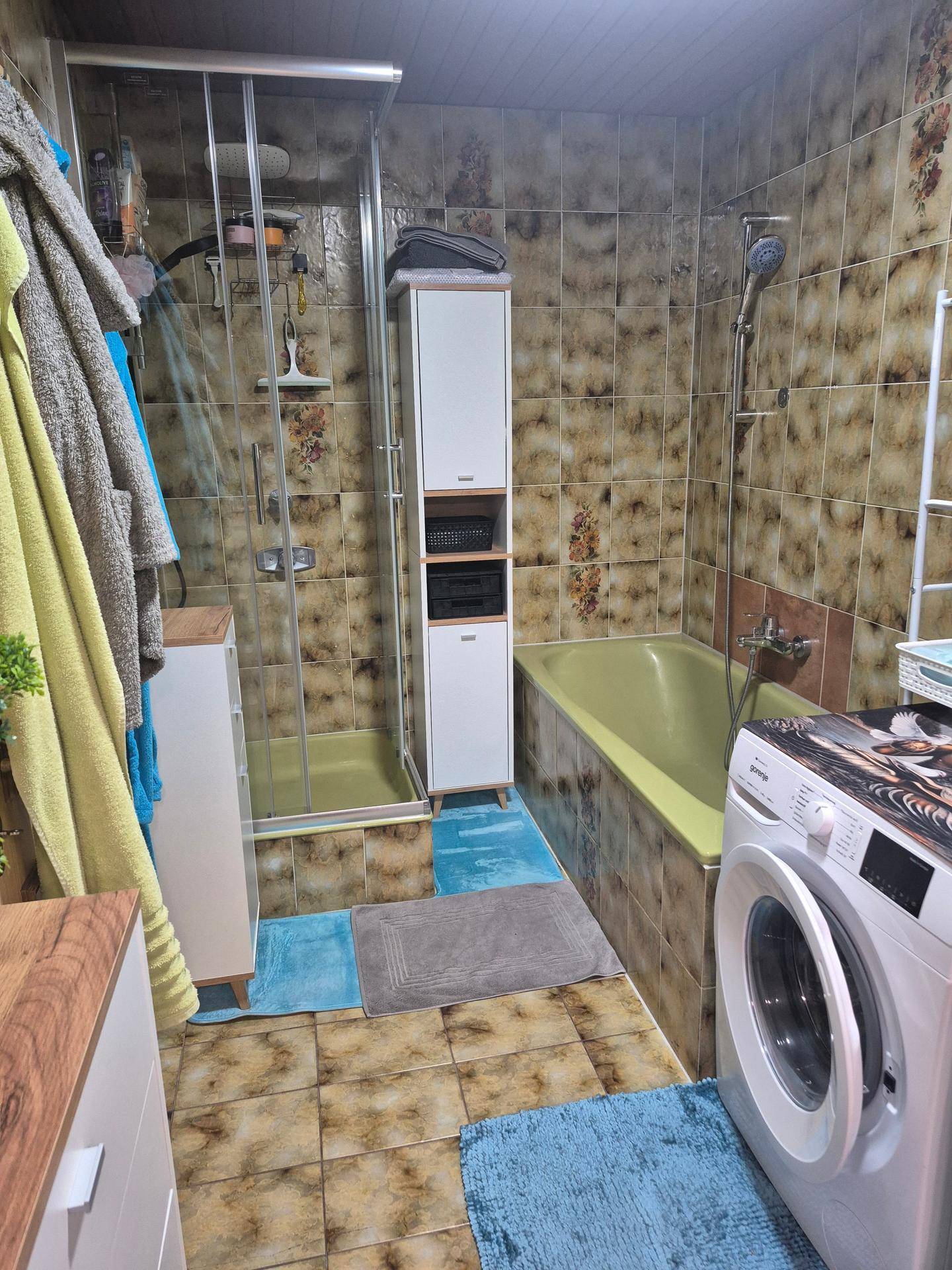 Badezimmer mit Duschkabine, Badewanne, gemusterten Fliesen und Waschmaschine.