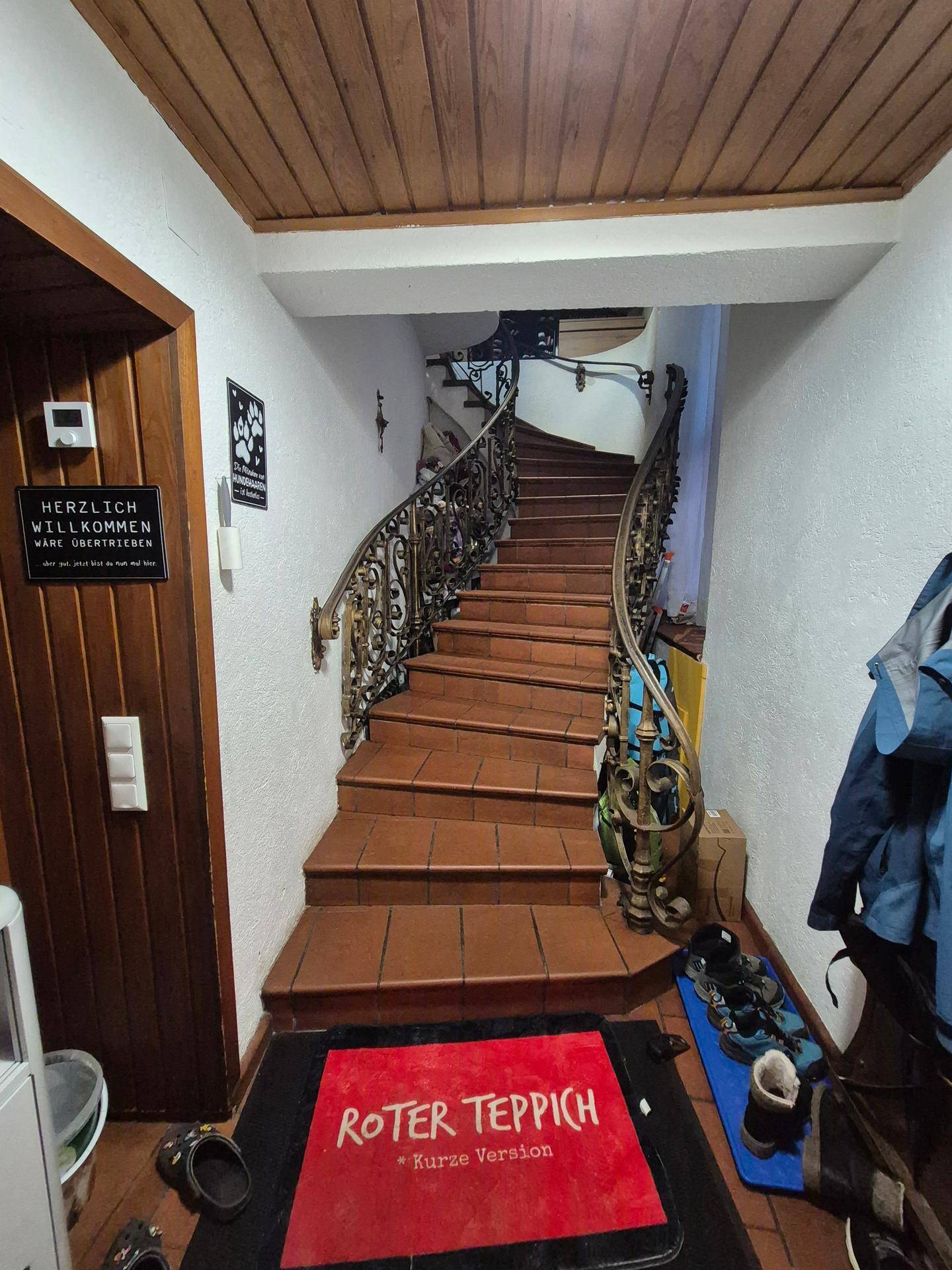Eingangsbereich mit Terrakottastufen, schmiedeeisernem Geländer und Holzdecke.