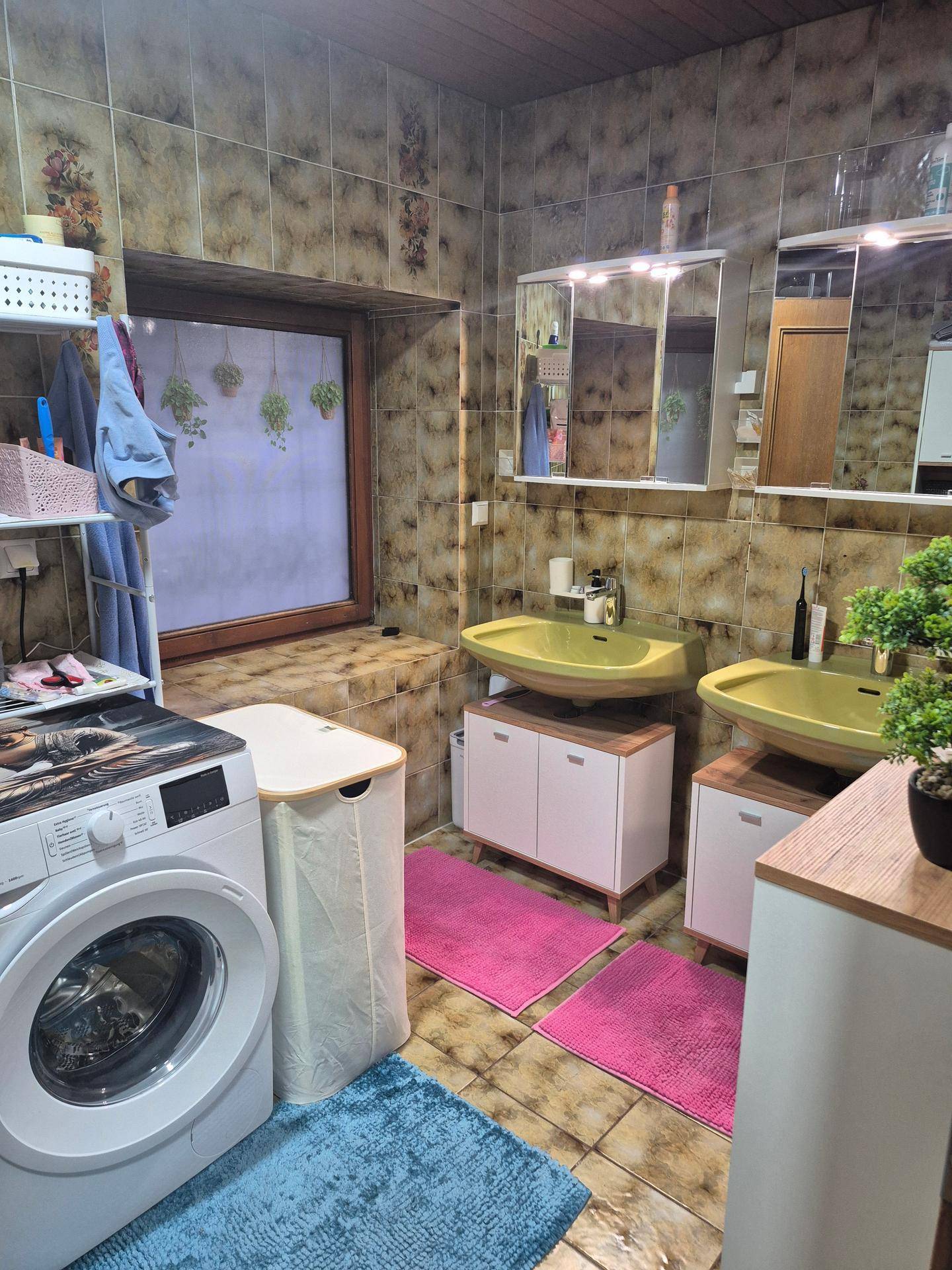 Badezimmer mit Doppelwaschbecken, gemusterten Fliesen, Waschmaschine und Fenster.