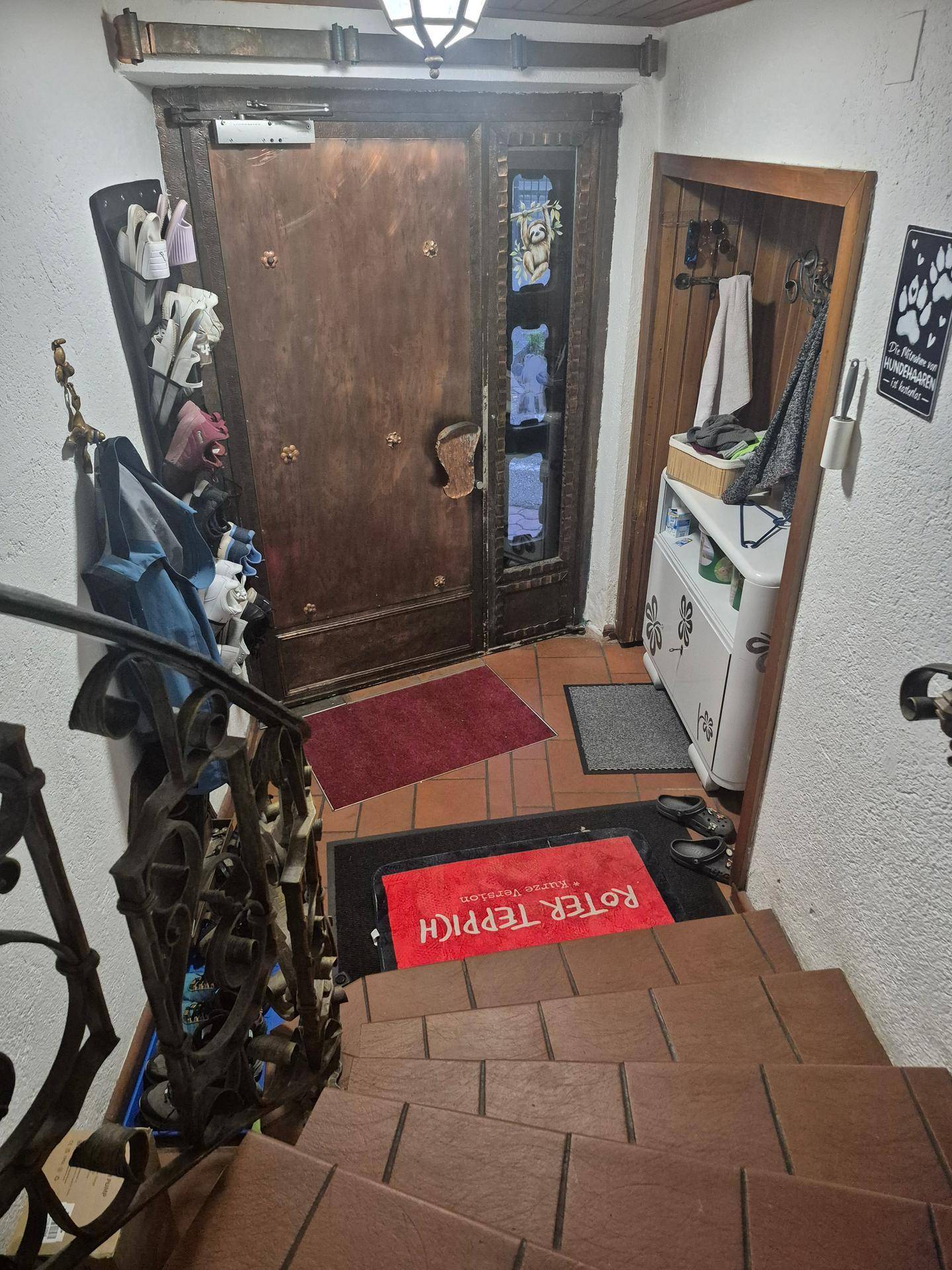 Eingangsbereich mit kunstvoller Holztür, Fliesenboden und Treppenaufgang.