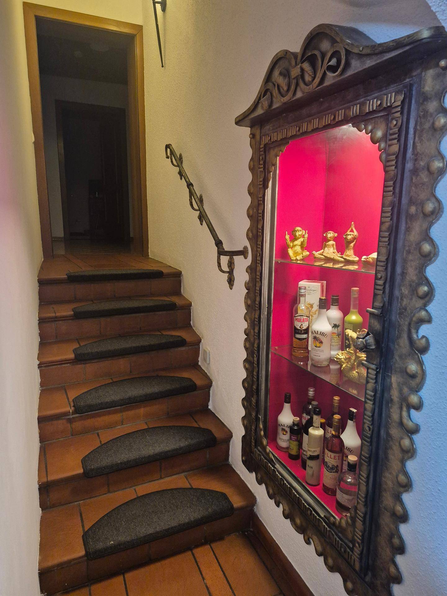 Treppenhaus mit Terrakottastufen, schmiedeeisernem Geländer und beleuchteter Vitrine.