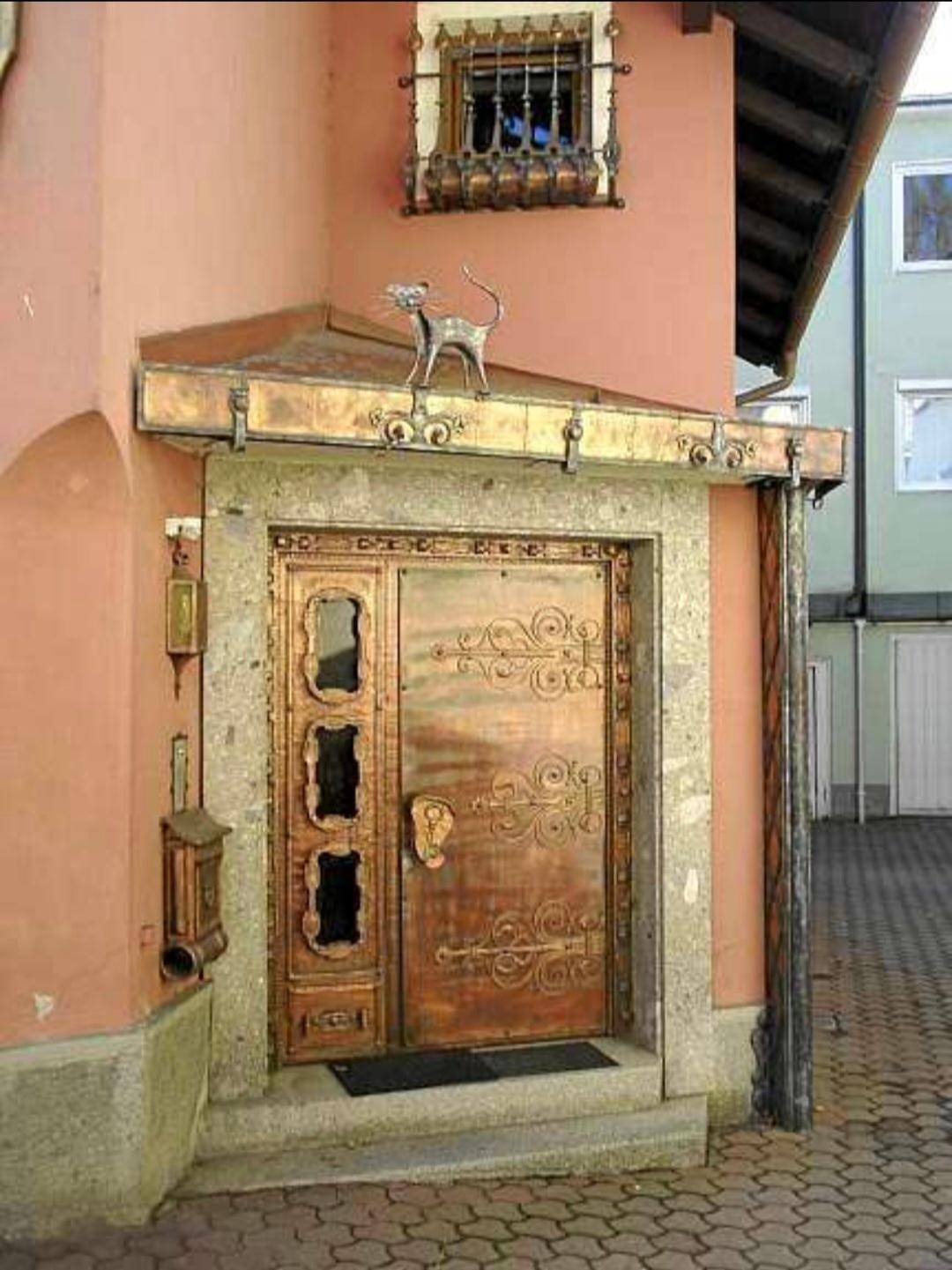 Historische Fassade mit kunstvoller Kupfertür, rosa Putz und dekorativem Fenstergitter.