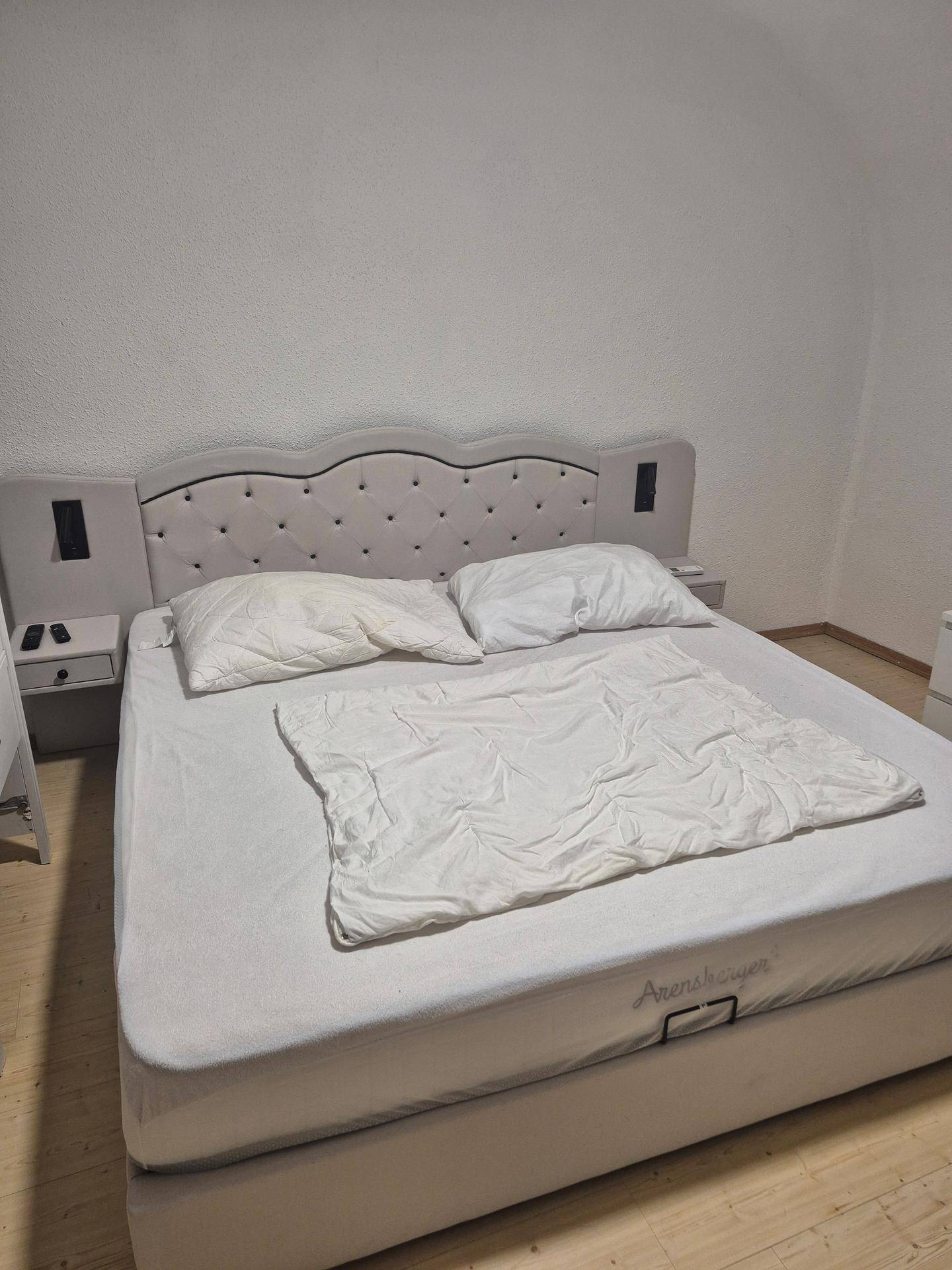 Helles Schlafzimmer mit großem Doppelbett, Holzboden und schlichten Wänden.