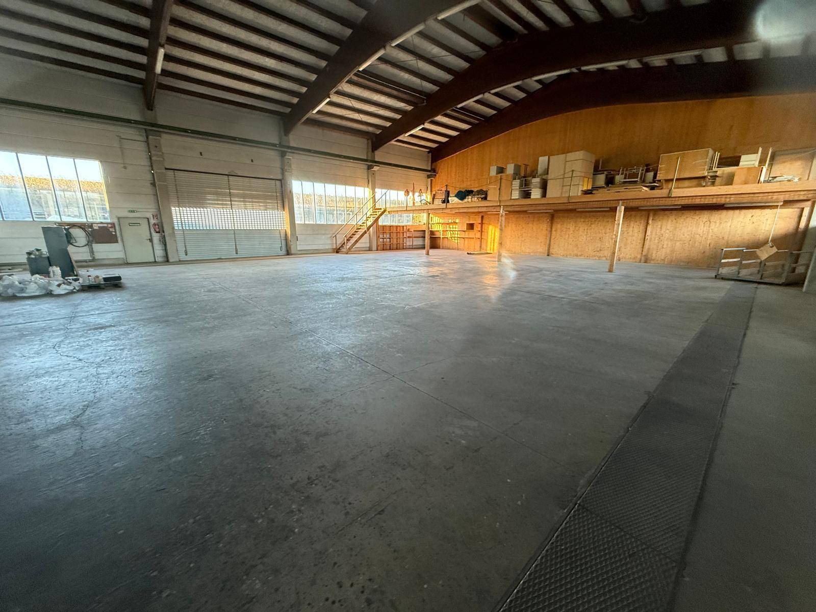 Weitläufige Industriehalle mit hohen Decken, Betonboden und einer erhöhten Plattform im Hintergrund.