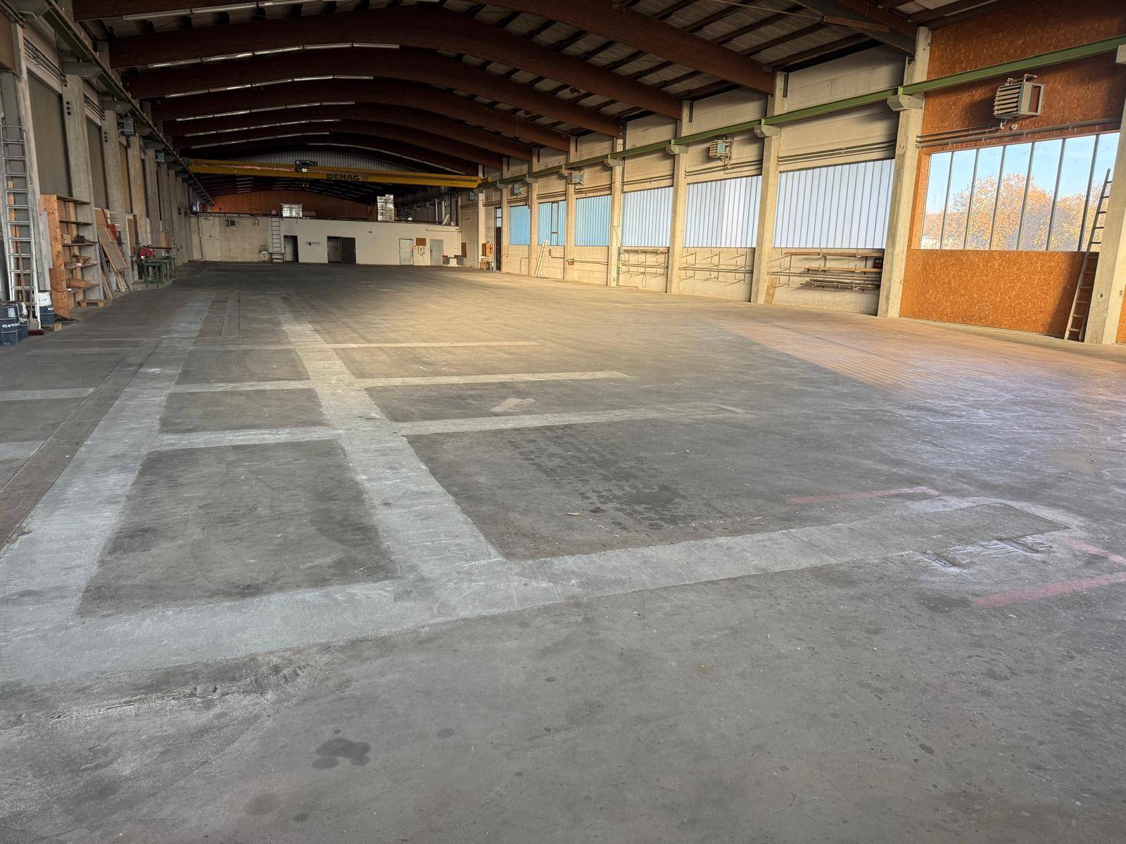 Geräumige Industriehalle mit Betonboden und hohen Decken, durch große Fenster gut mit Tageslicht versorgt.