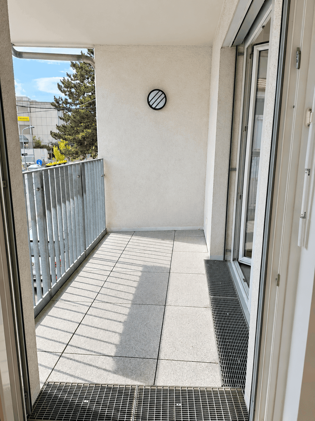 Heller Balkon mit Fliesenboden und Metallgeländer, bietet einen Blick ins Grüne.