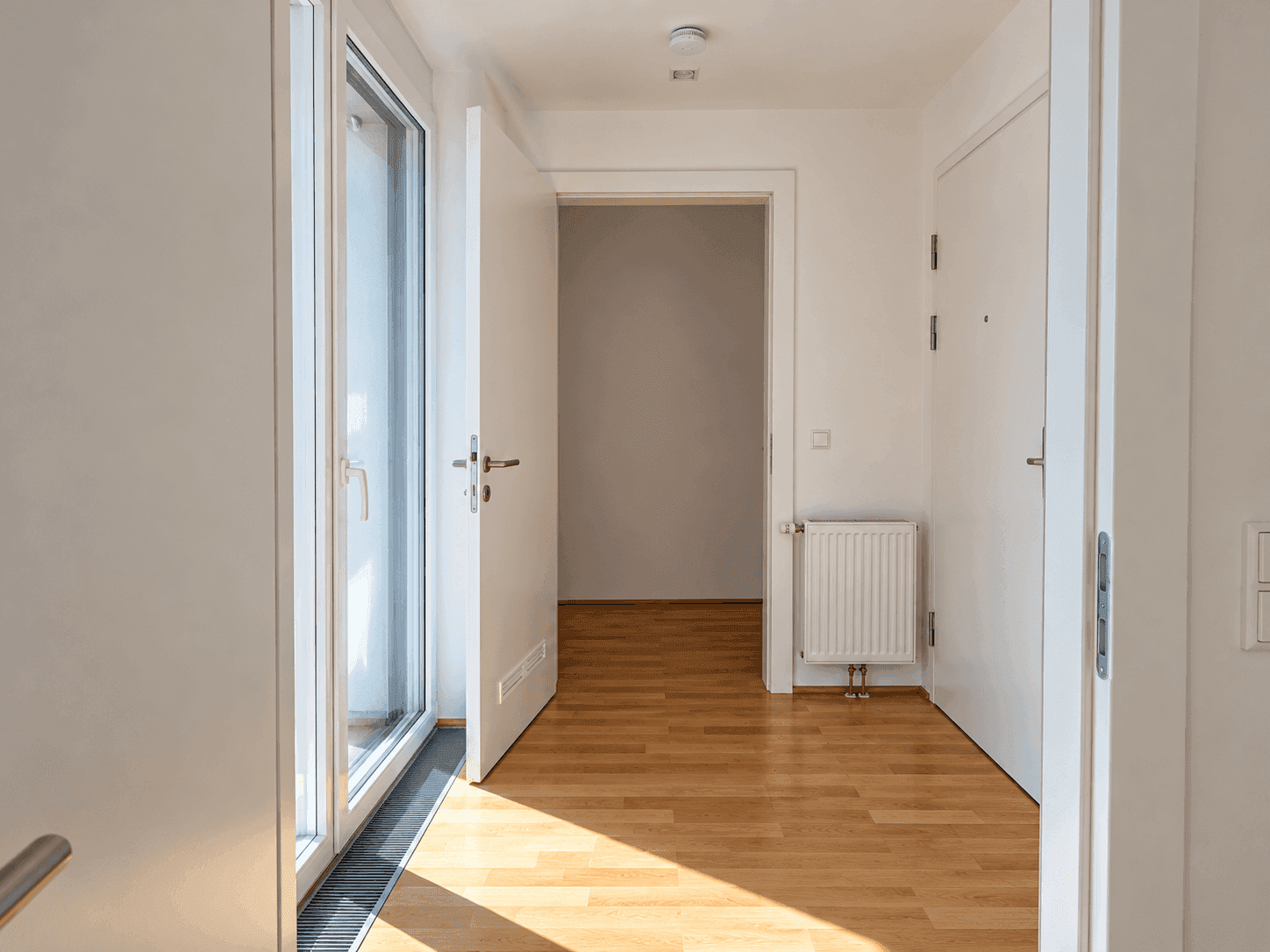 Heller Flur mit Holzparkettboden, weiß gestrichenen Wänden und Zugang zu weiteren Räumen.
