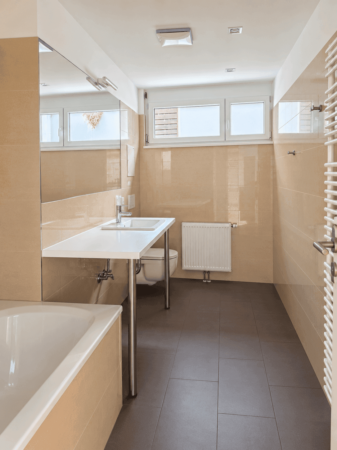 Helles Badezimmer mit Fenster, beigefarbenen Fliesen, Einzelwaschbecken und WC.