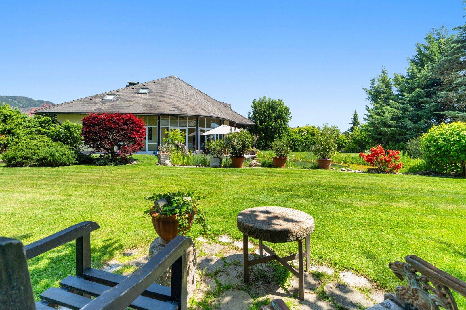 Weitläufiger grüner Garten mit Rasenfläche, Sitzgelegenheiten und Blick auf das Haus.