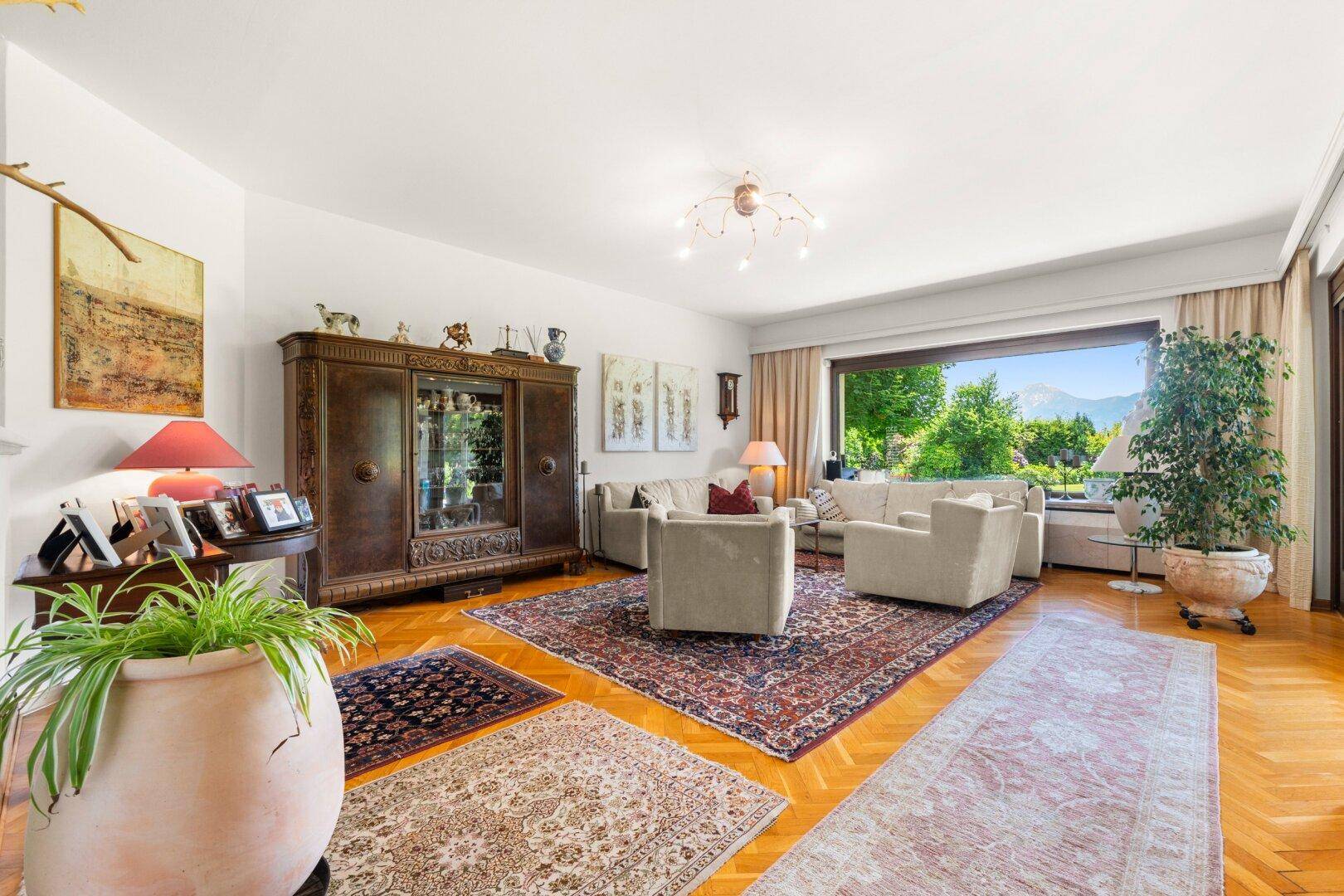 Geräumiges Wohnzimmer mit Parkettboden, traditionellen Möbeln und großem Fenster mit Gartenblick.