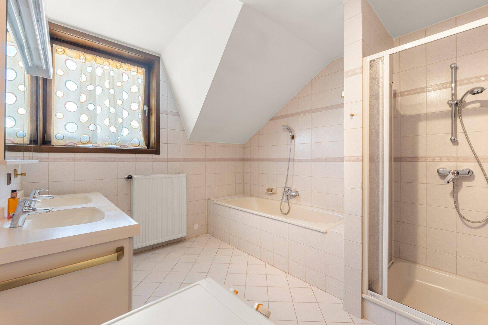 Badezimmer im Dachgeschoss mit Badewanne, Dusche, Doppelwaschbecken und Fenster.