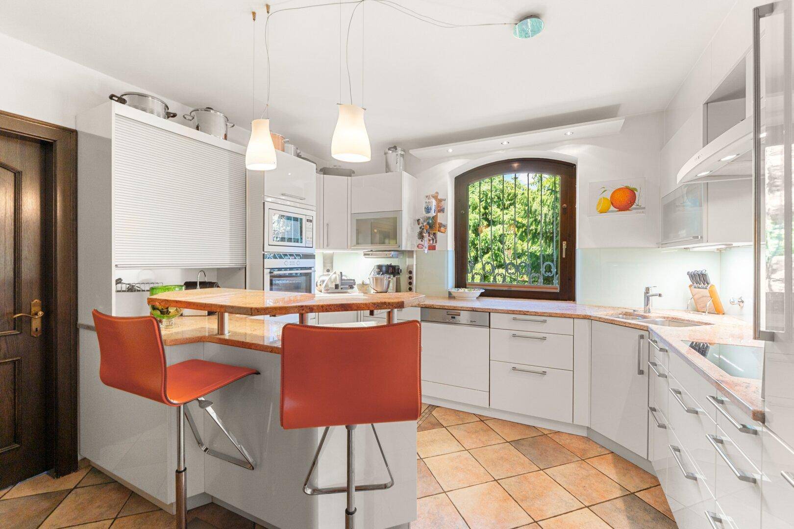 Moderne Küche mit weißen Schränken, Kücheninsel und einem Fenster mit Blick ins Grüne.