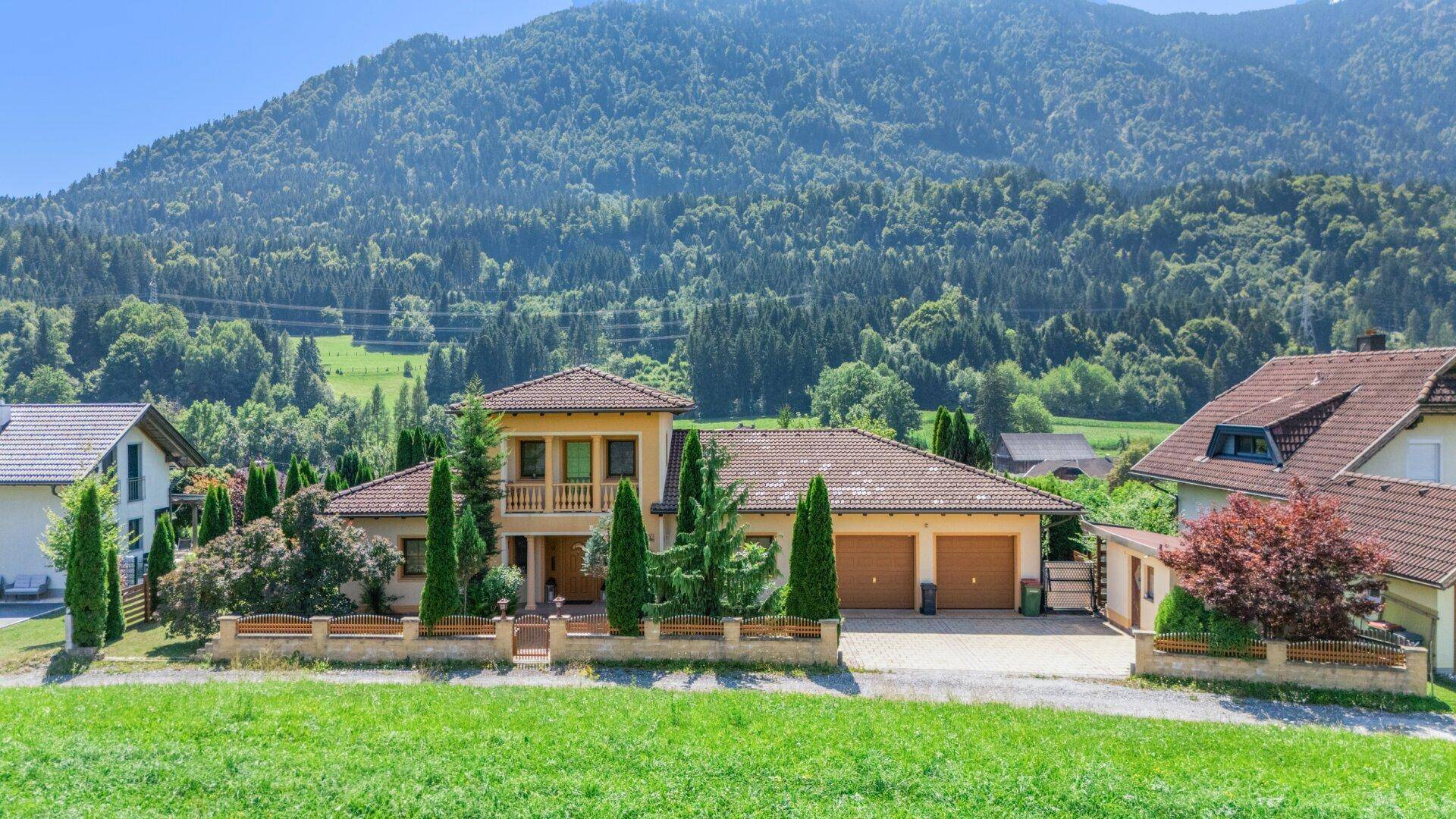 Haus mit traditioneller Architektur und Doppelgarage, eingebettet in eine grüne Landschaft mit Bergblick.