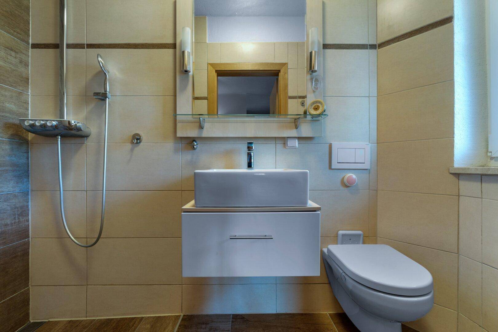 Modernes Badezimmer mit beigefarbenen Fliesen, wandhängendem WC und ebenerdiger Dusche.