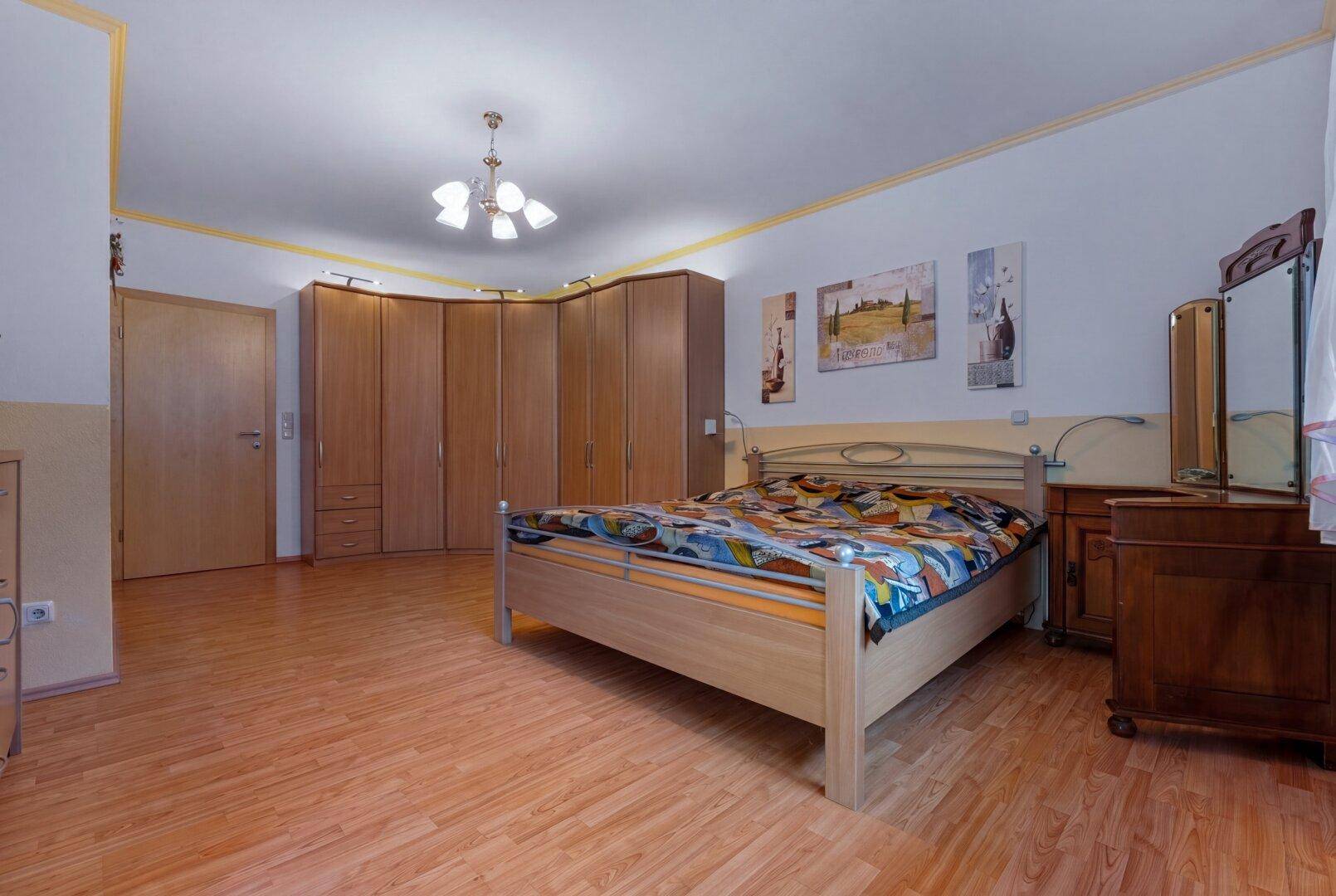 Schlafzimmer mit hellem Laminatboden, großem Eckkleiderschrank und gemütlichem Doppelbett.