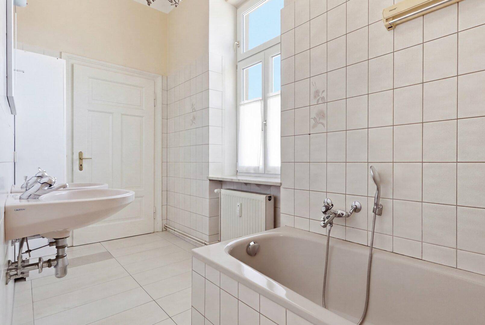 Helles Badezimmer mit Badewanne, Waschbecken, Fliesen und einem Fenster.