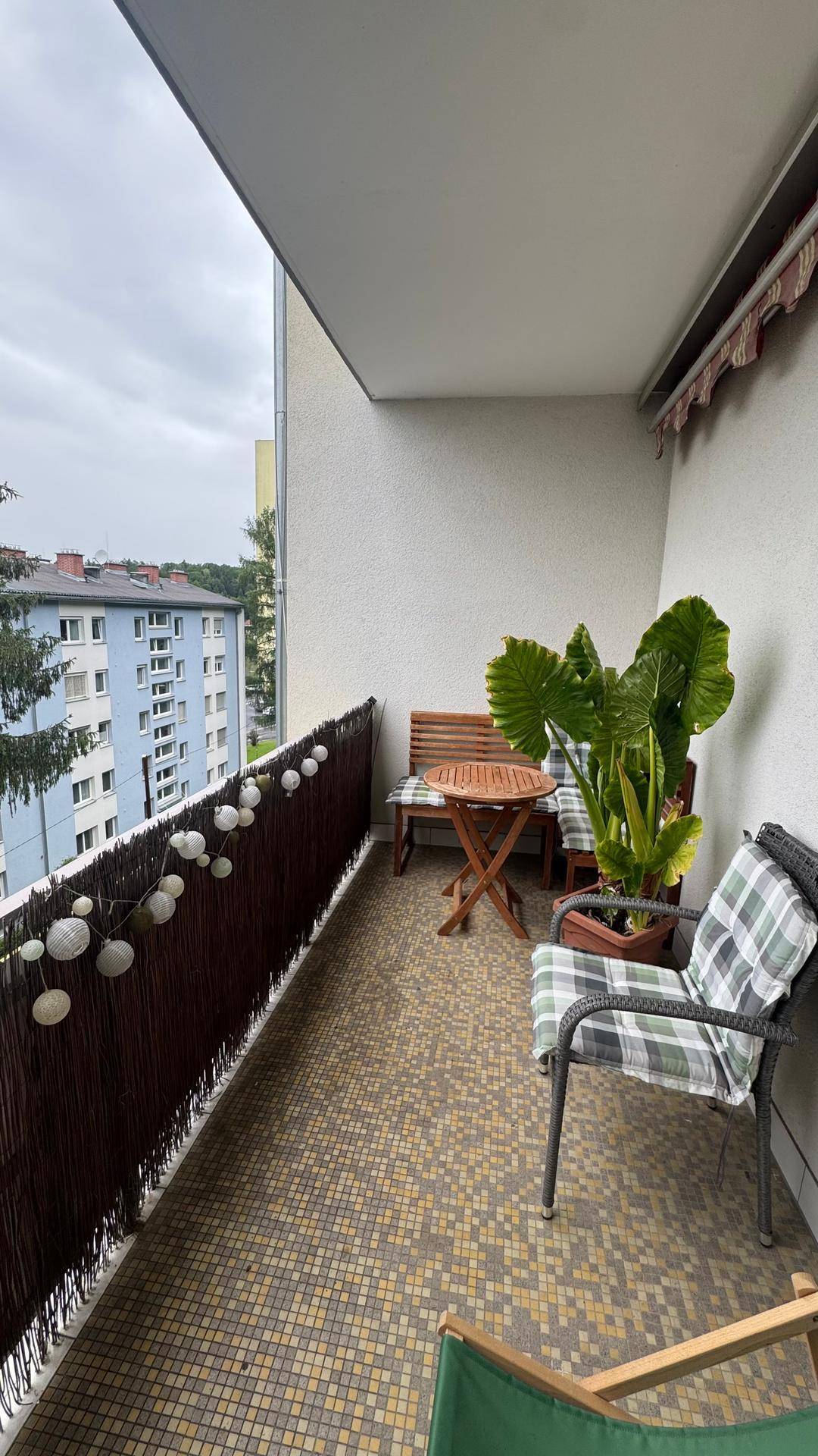 Gemütlicher Balkon mit Sitzgelegenheiten, Pflanzen und Blick auf die umliegenden Gebäude.