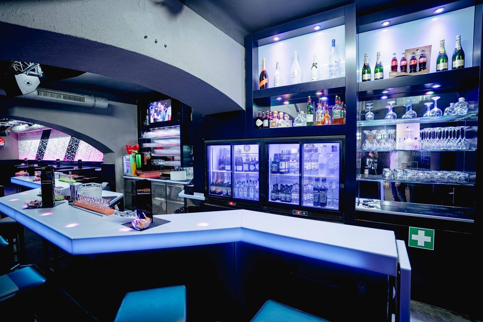 Beleuchtete Bar mit einer Auswahl an Getränken, Gläsern und einem Erste-Hilfe-Kasten, bereit für den Betrieb.