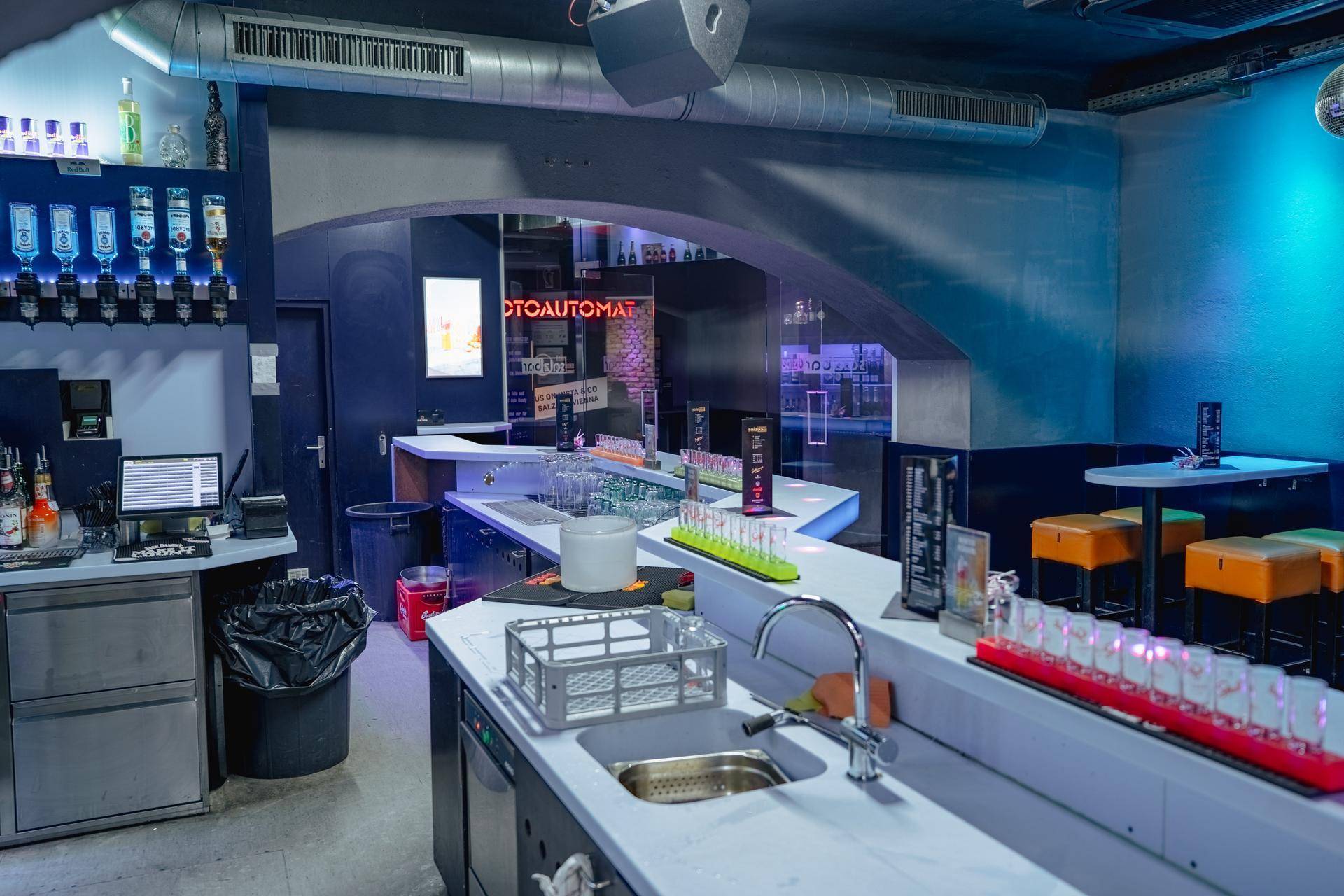 Servicebereich hinter der Bar mit Spülbecken, Arbeitsflächen und Mülleimern, für effizienten Barbetrieb.