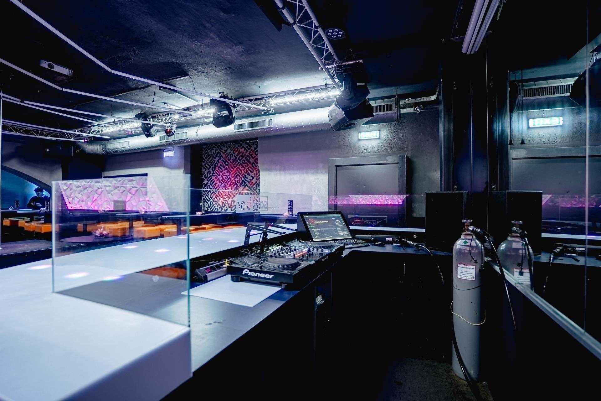 Nahaufnahme des DJ-Pults mit professioneller Ausrüstung, Laptops und einem Sauerstofftank im Hintergrund.