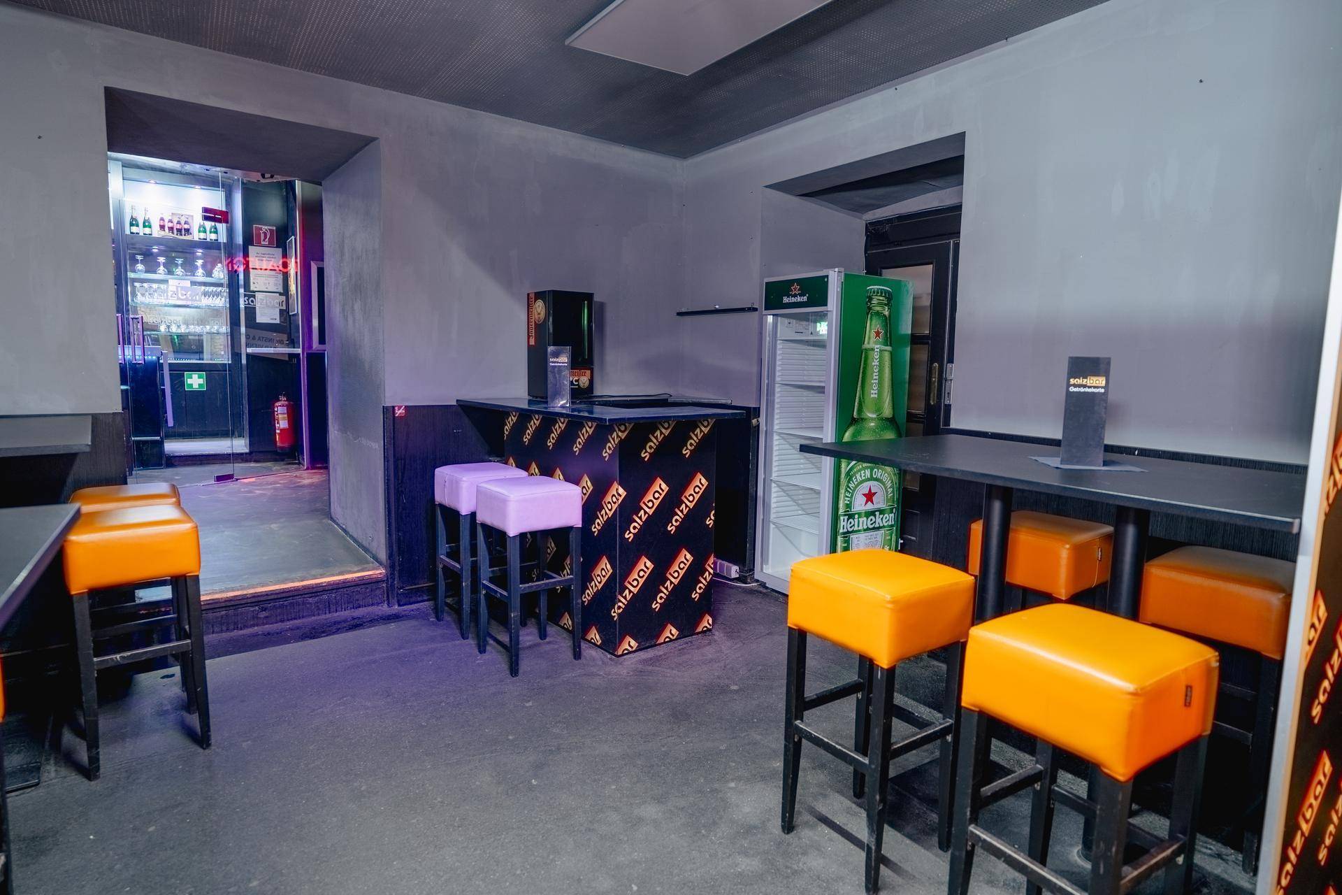 Lounge-Bereich mit Tischen, Hockern und einem Getränkekühlschrank, bereit für Gäste in entspannter Atmosphäre.