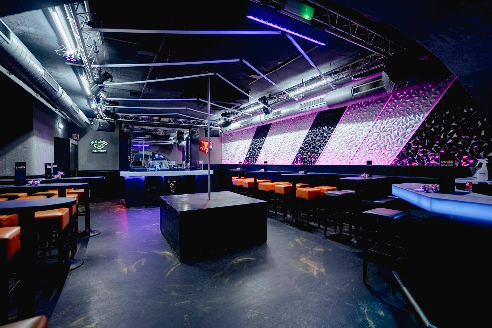 Geräumiger Clubbereich mit Tanzstange, DJ-Pult und Sitzgelegenheiten, akzentuiert durch moderne Wandpaneele und Beleuchtung.