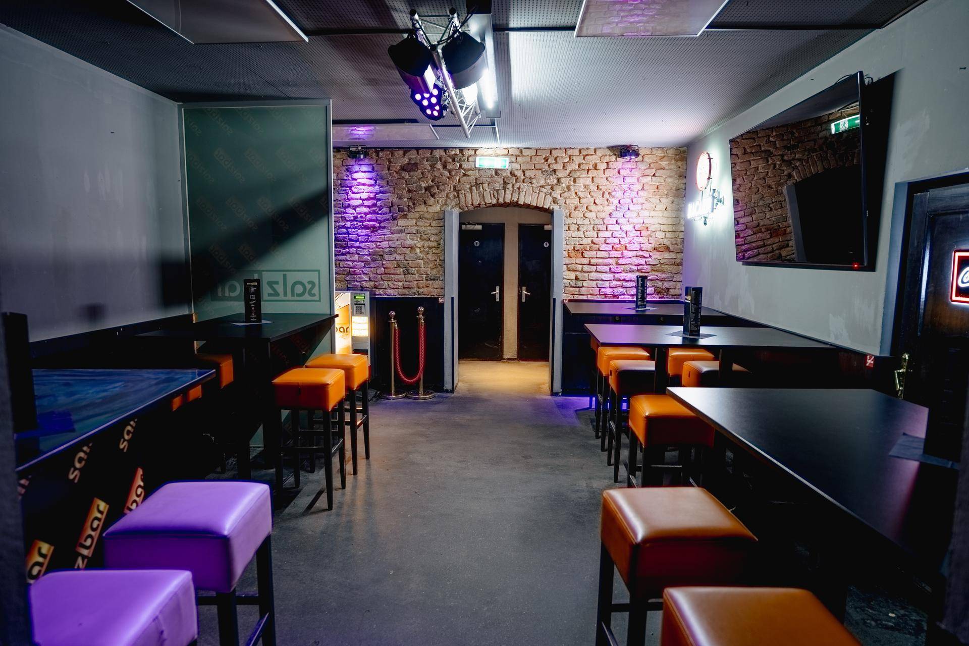 Lounge-Bereich mit Tischen und orangefarbenen Hockern, akzentuiert durch eine freigelegte Ziegelwand und indirekte Beleuchtung.