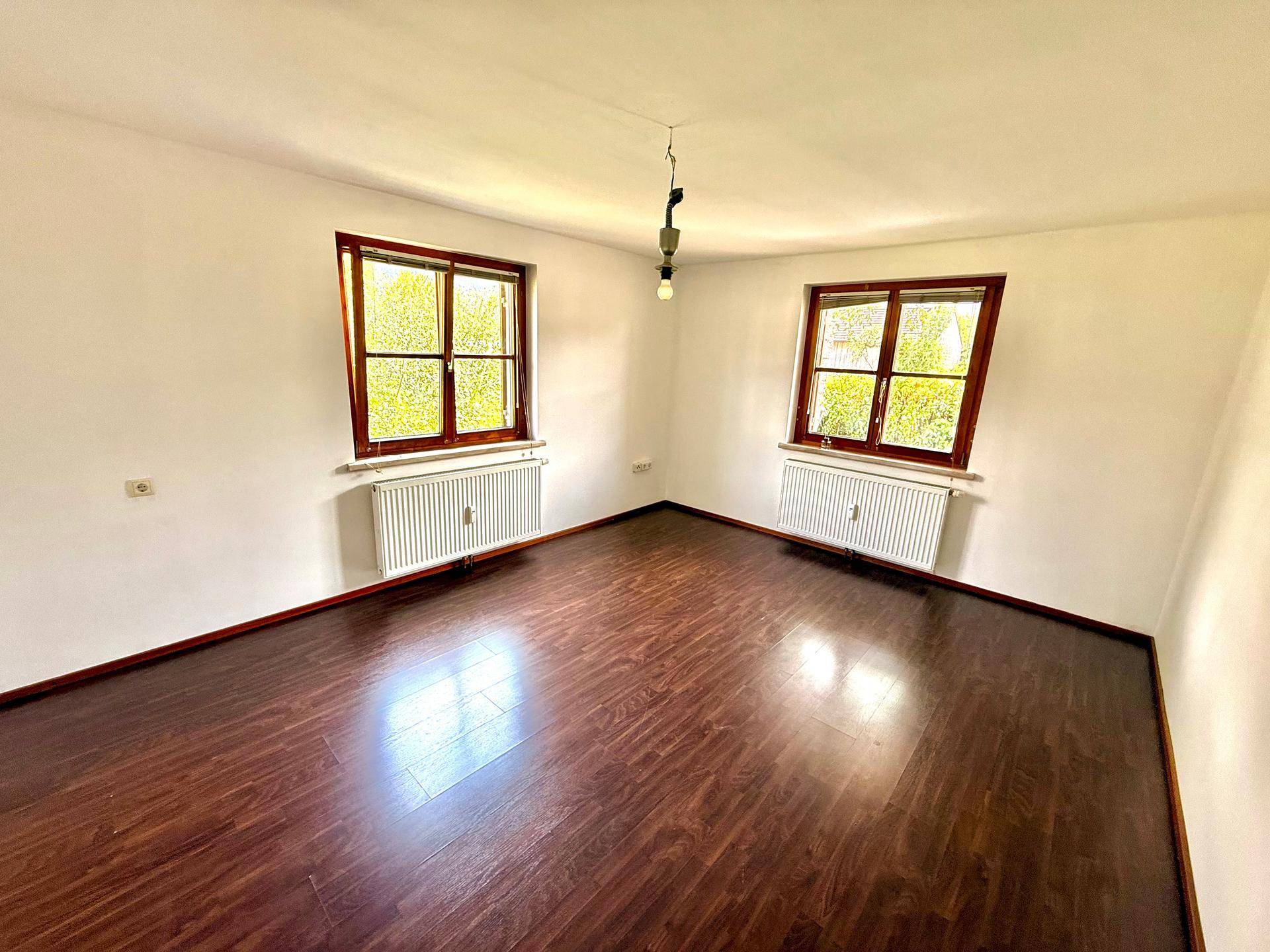 Geräumiges Zimmer mit zwei Fenstern und dunklem Laminatboden, ideal als Wohn- oder Schlafzimmer.