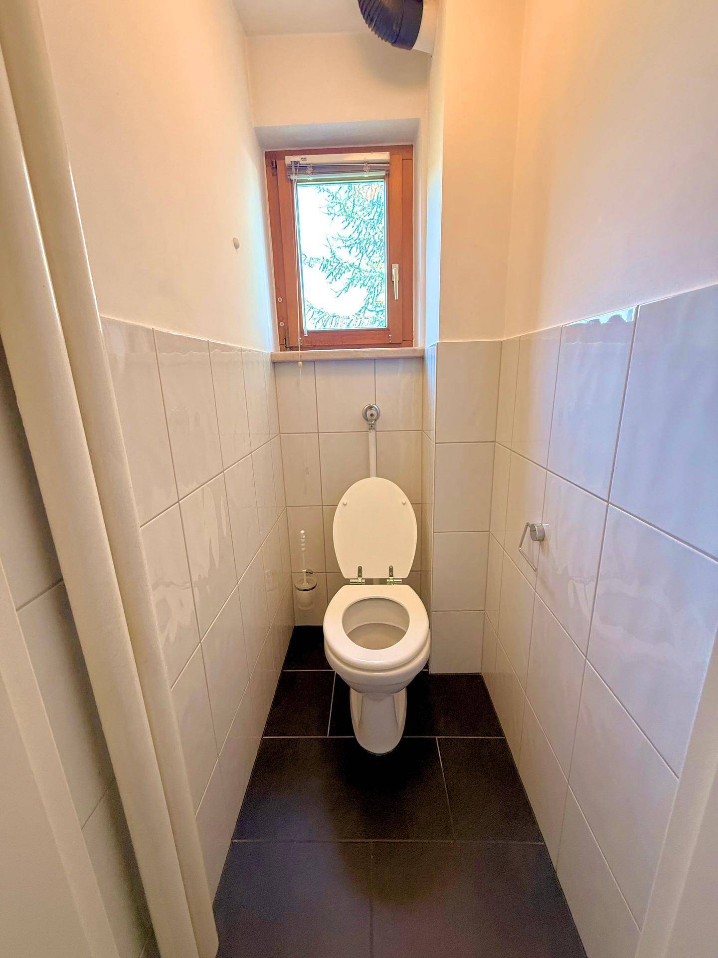 Separates WC mit Fenster und weißen Fliesen, ausgestattet mit einer Standardtoilette.