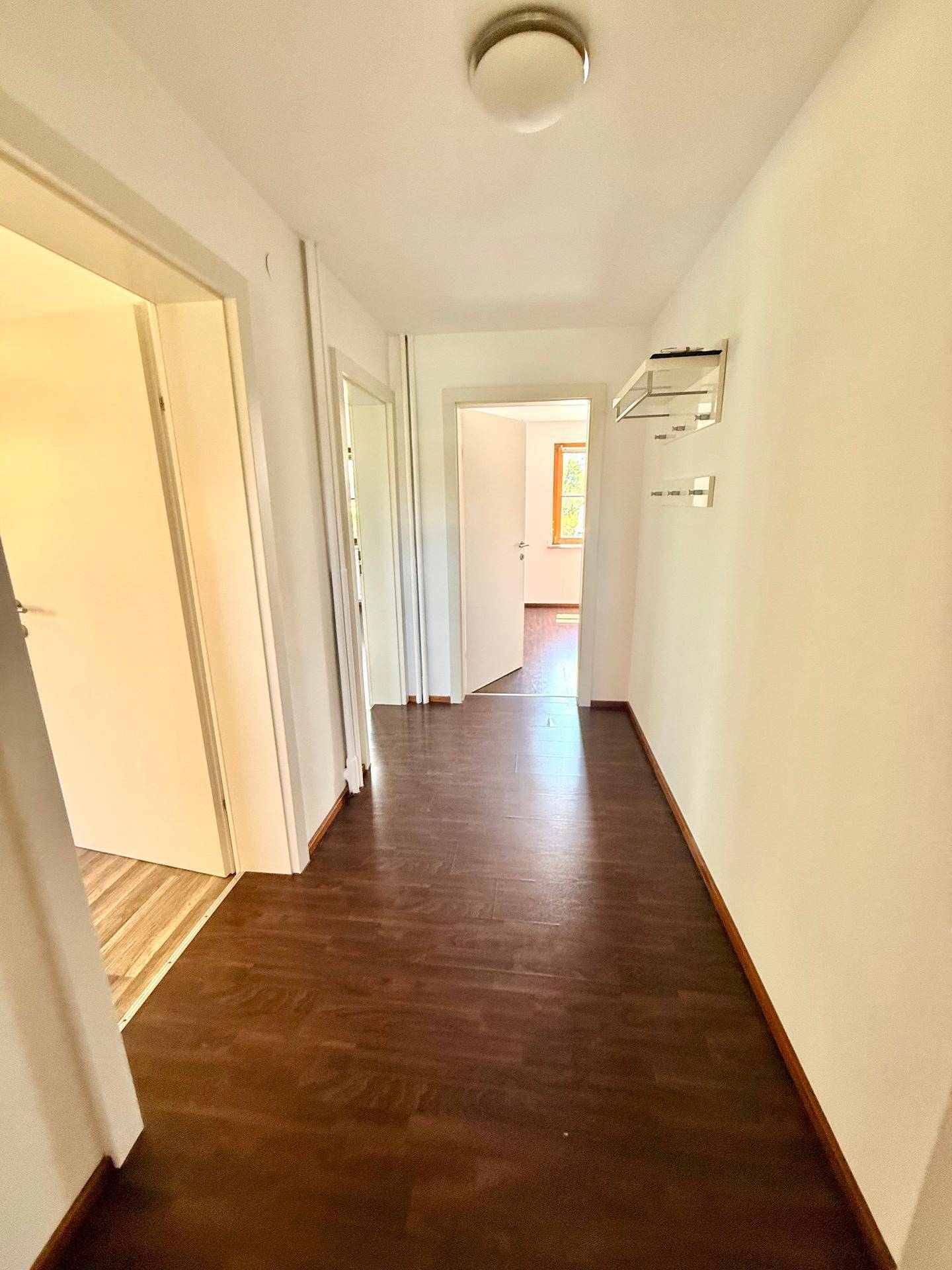 Langer Flur mit dunklem Laminatboden und weiß gestrichenen Wänden, der die Räume miteinander verbindet.