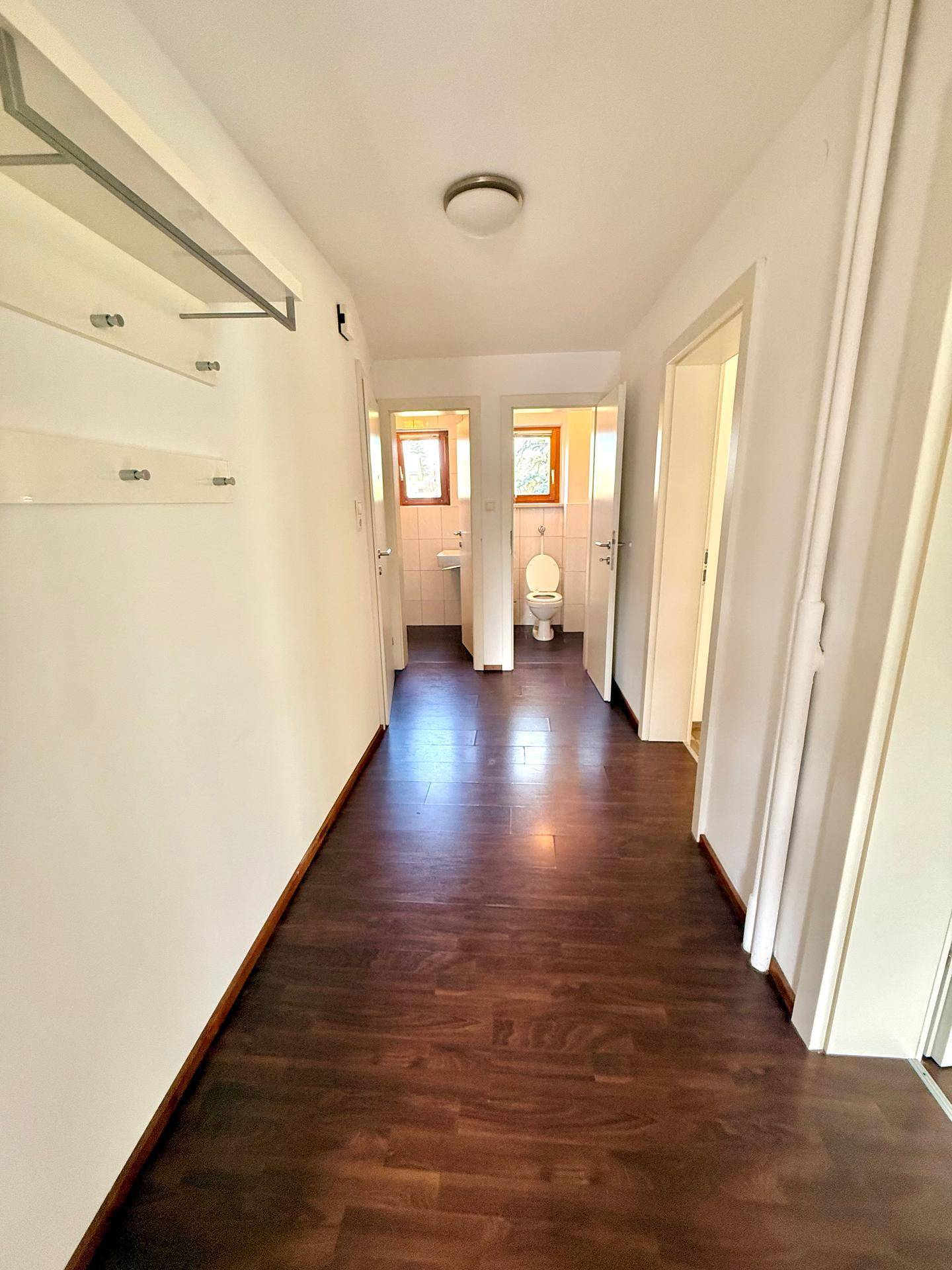 Heller Flur mit dunklem Laminatboden, der zu den verschiedenen Zimmern und dem Badezimmer führt.